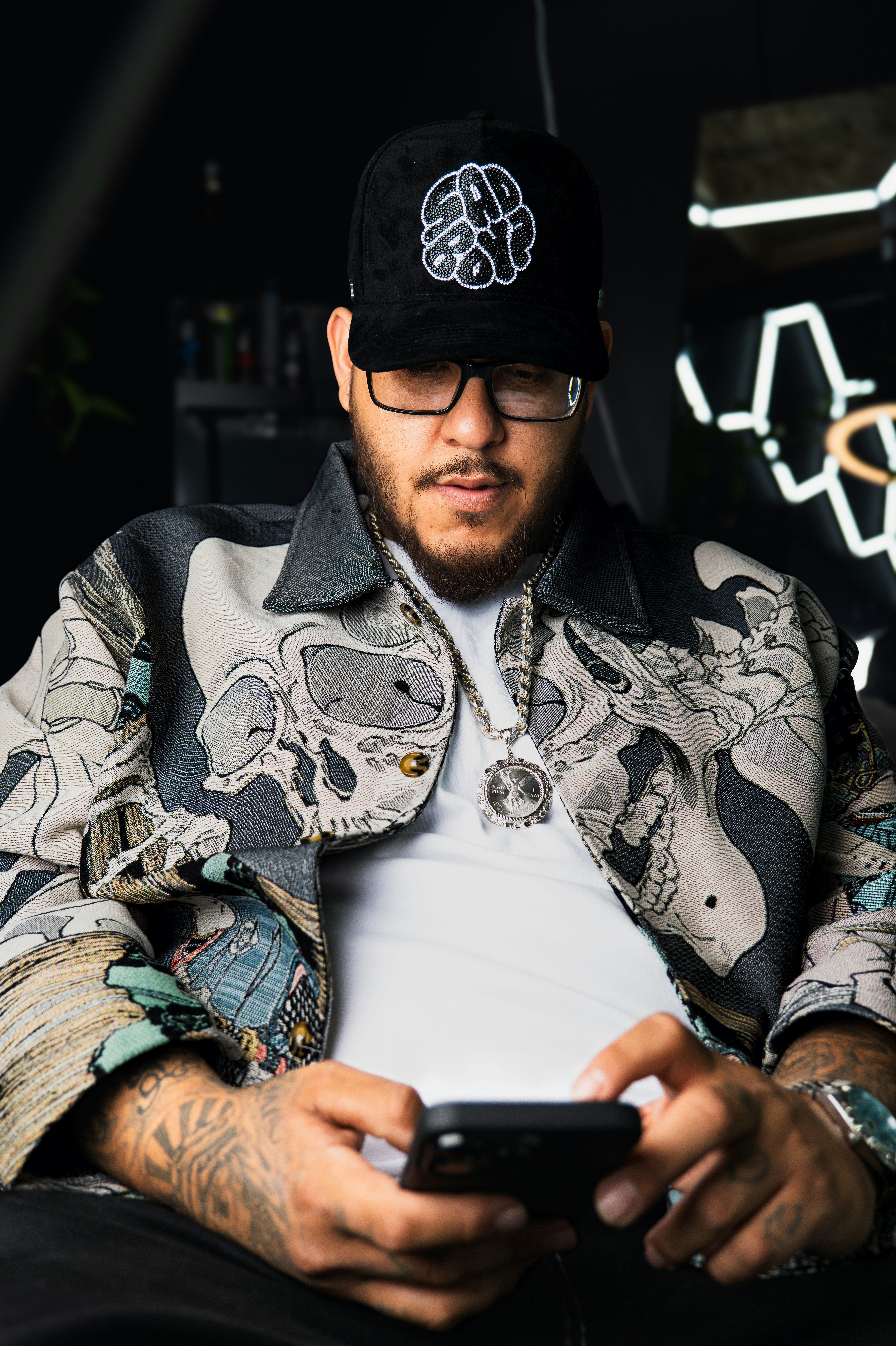 A man with a beard and glasses using a smartphone in a patterned jacket