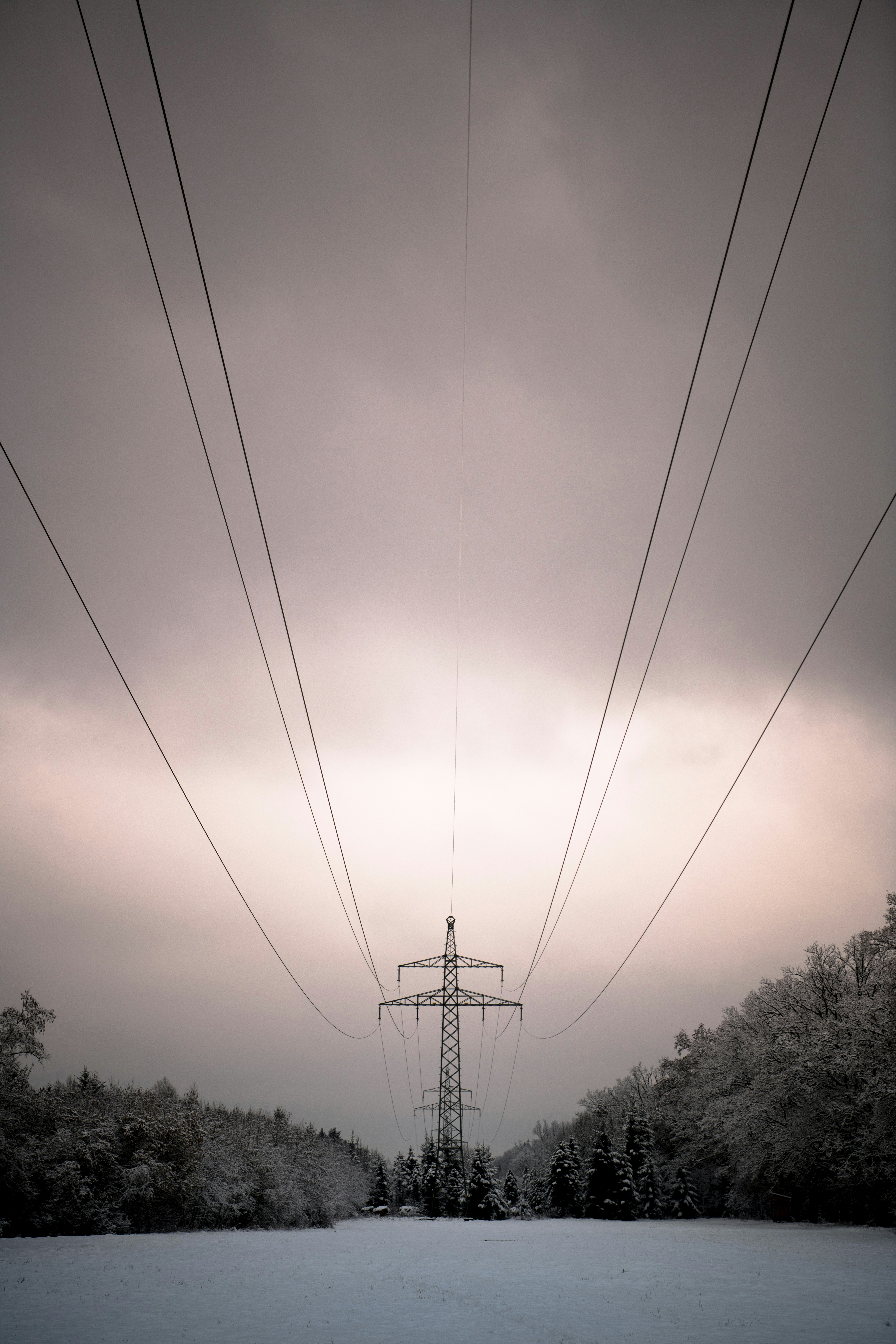 Ein hoher metallener Strommast mit Stromleitungen über einem verschneiten Feld und Wald