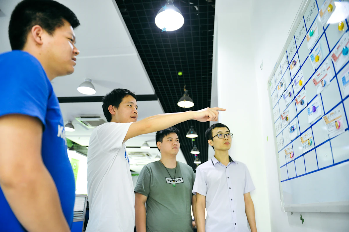 A man pointing at one card on a wall-sized planning board while three colleagues follow where he is pointing