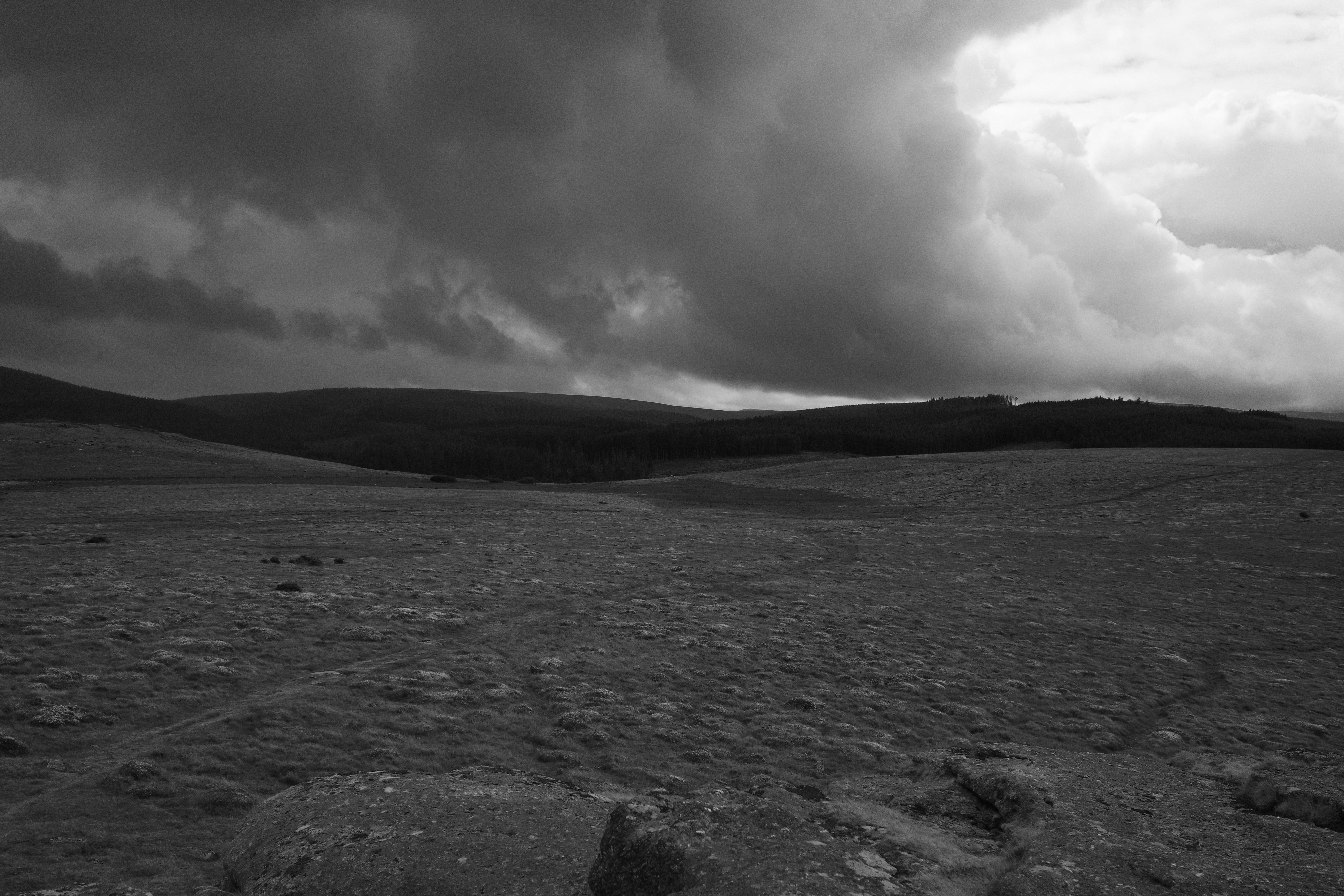 A black and white landscape of rolling hills under a dark stormy sky