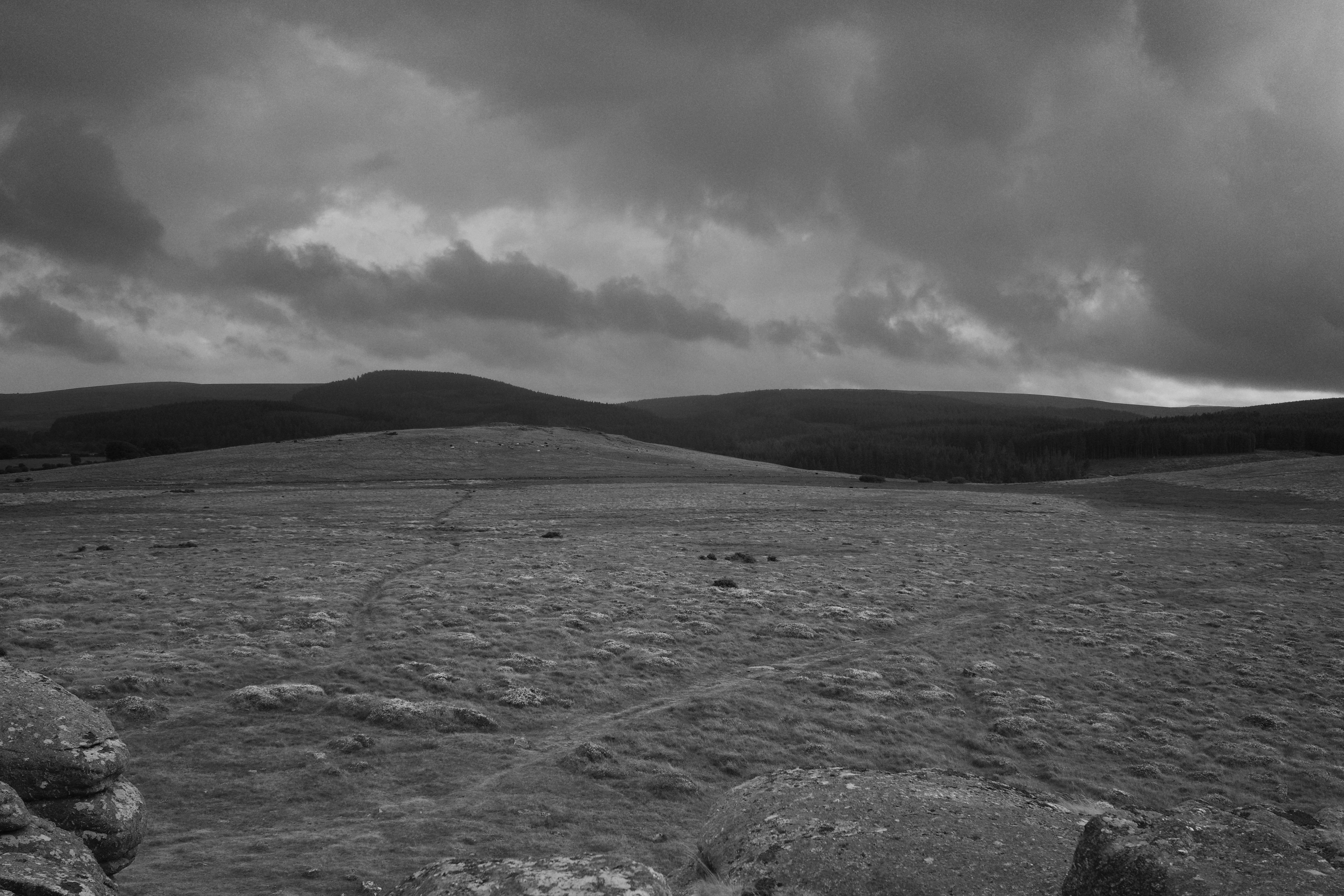 A vast moorland under a dark cloudy sky with distant rolling hills