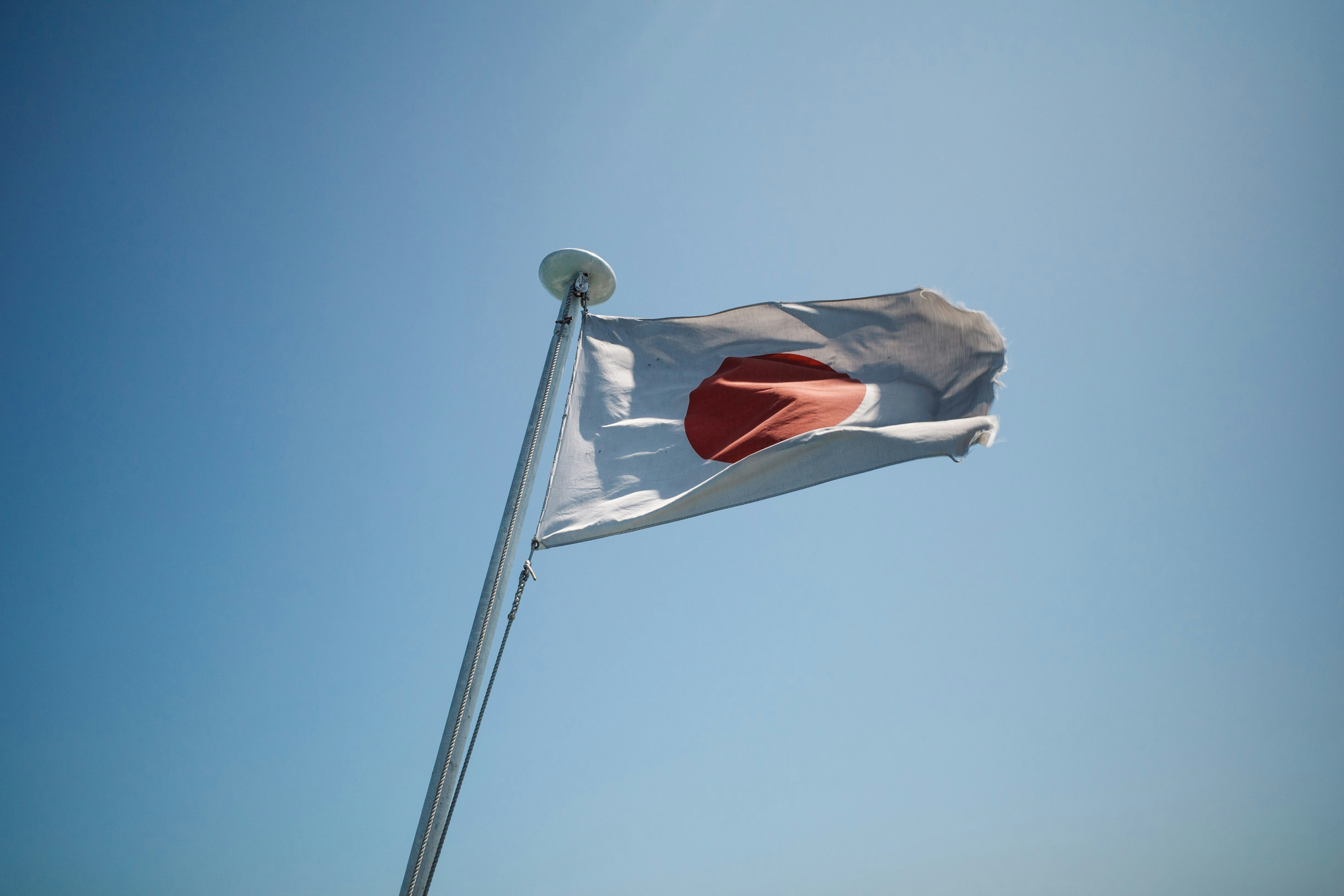 The national flag of Japan waving on a pole against a clear blue sky
