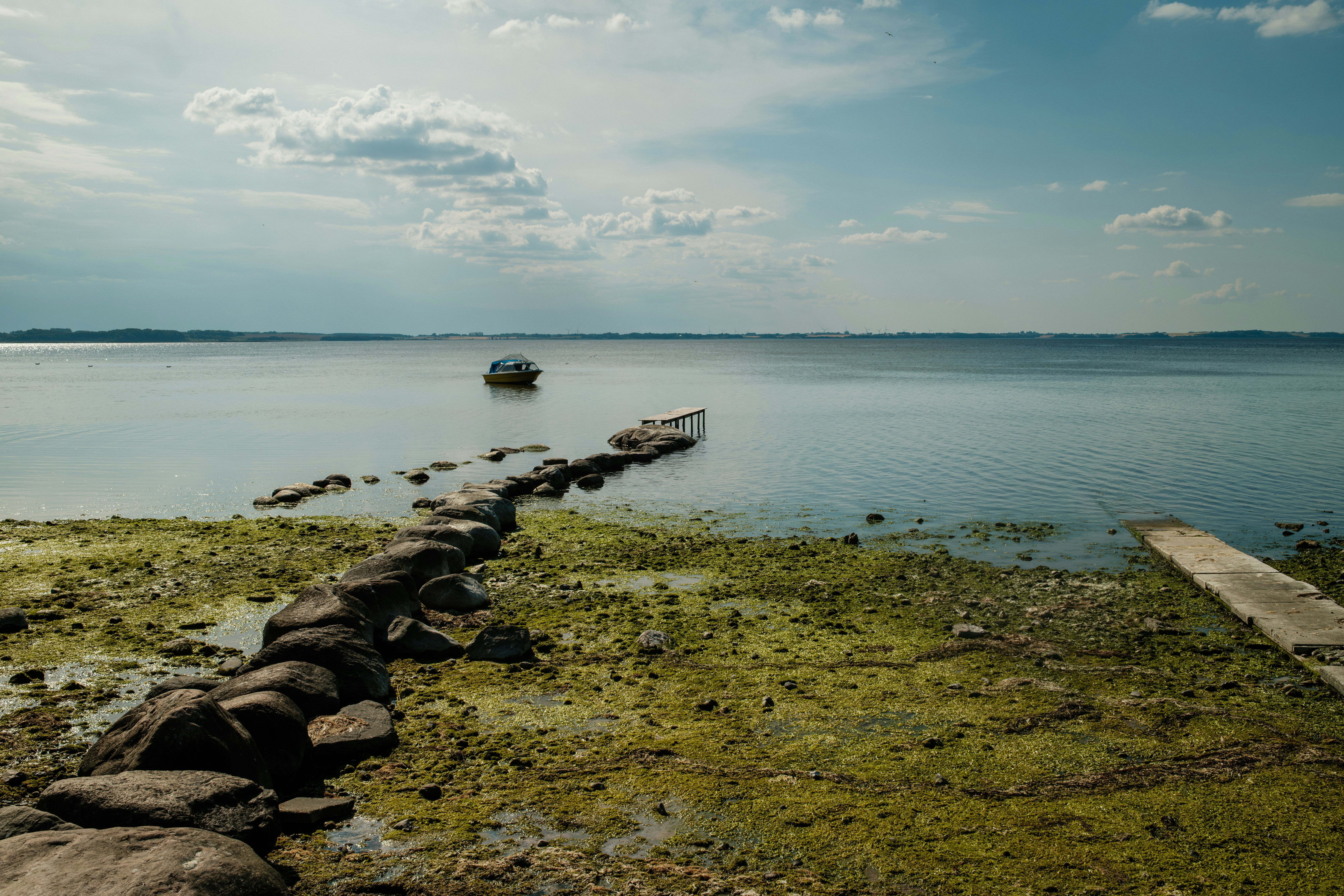 A small boat anchored near a stone pier extending into a calm lake