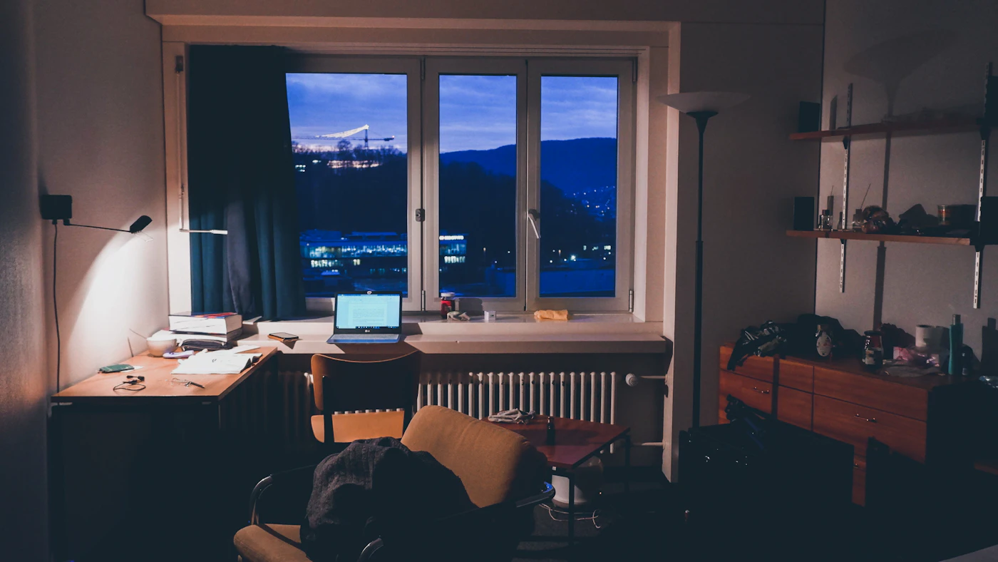 Escritorio en casa de noche con un portátil encendido junto a la ventana