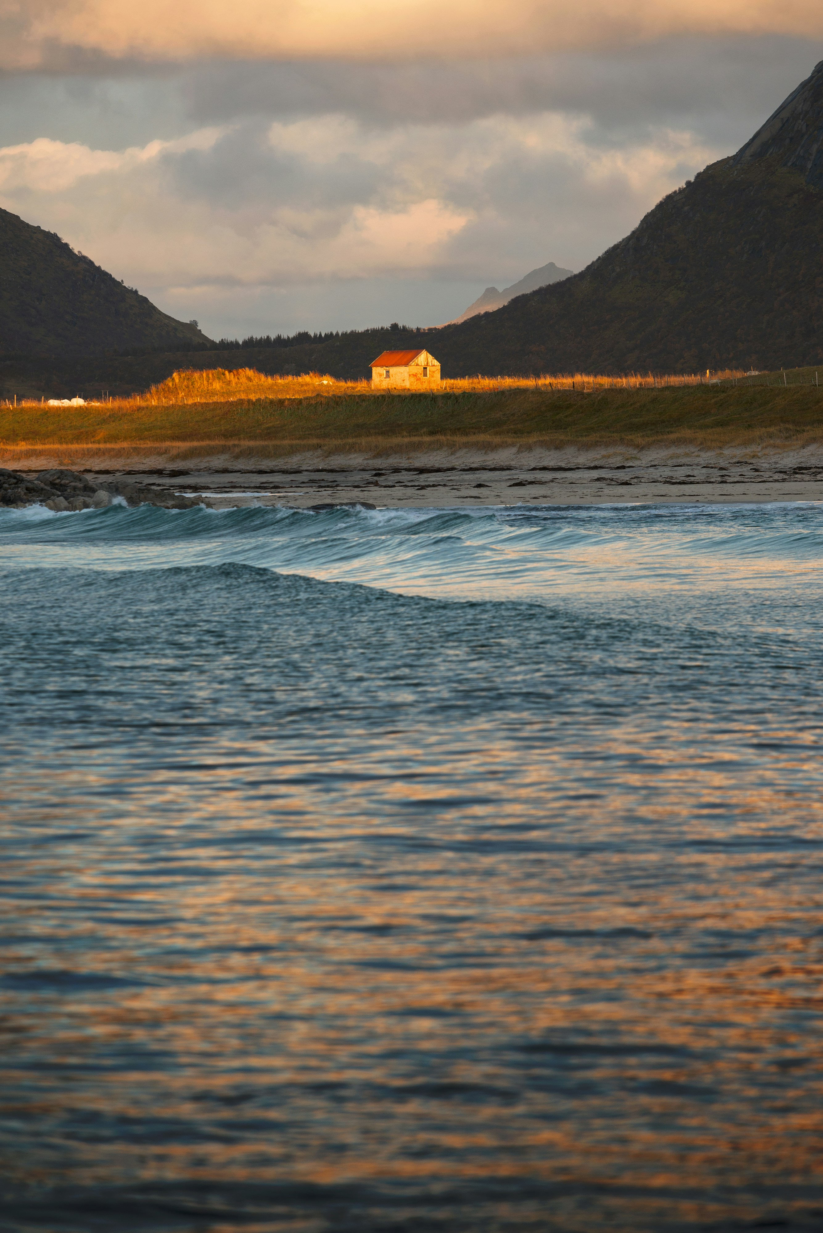 A small cabin on a grassy hill above a beach at golden hour