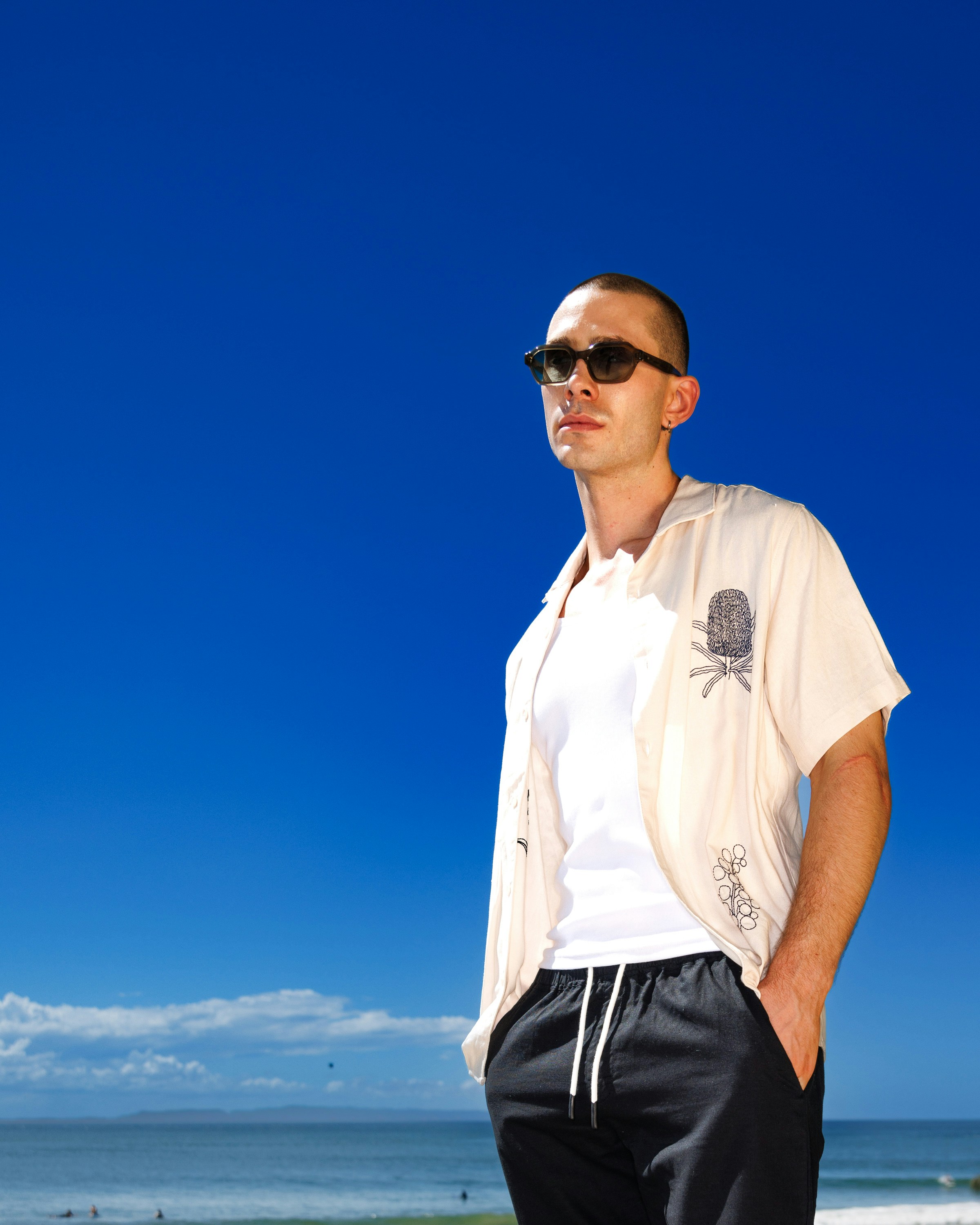 A man in sunglasses and a cream shirt against a bright blue sky