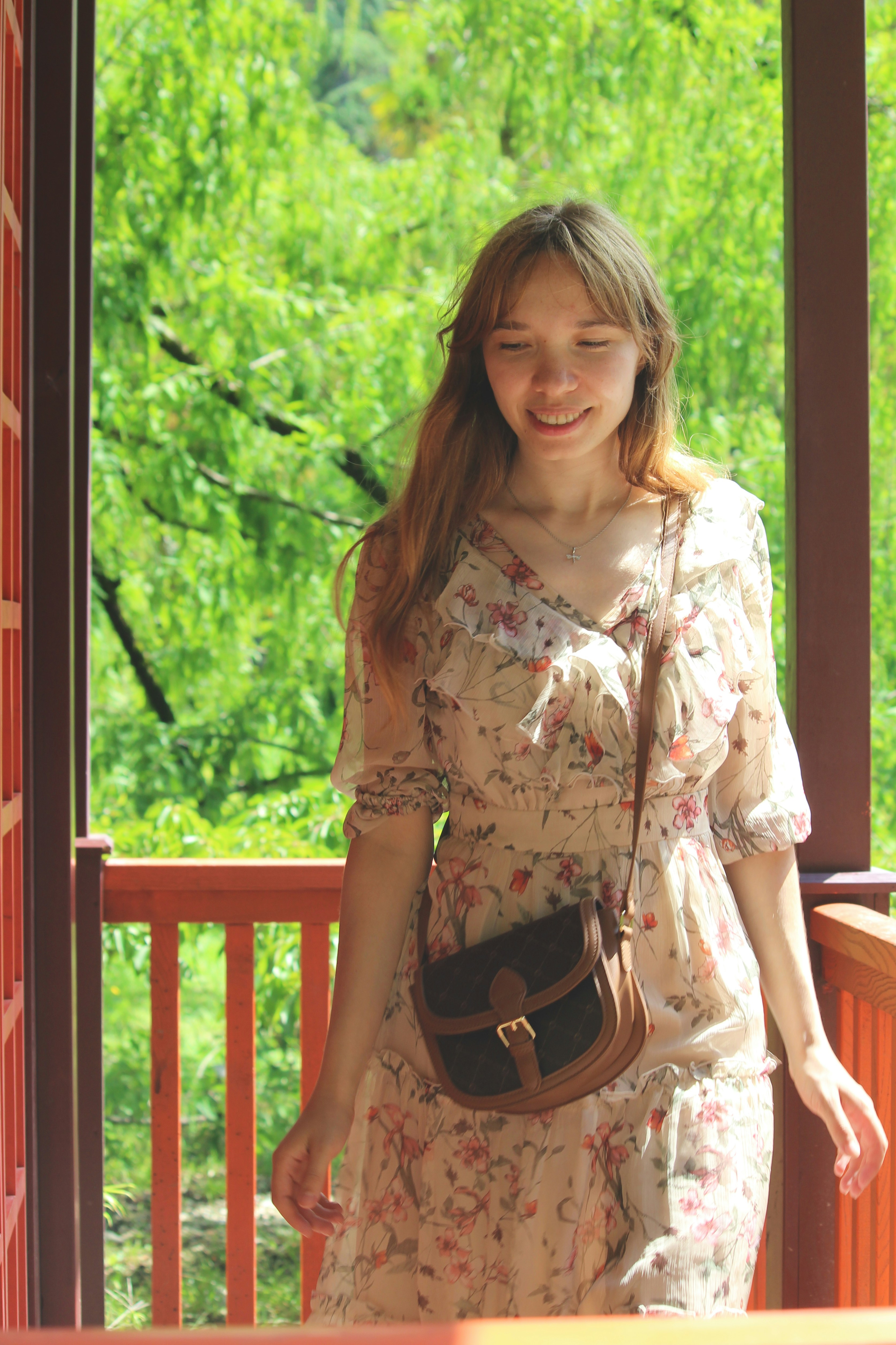 A woman in a floral dress with a brown crossbody bag on a porch