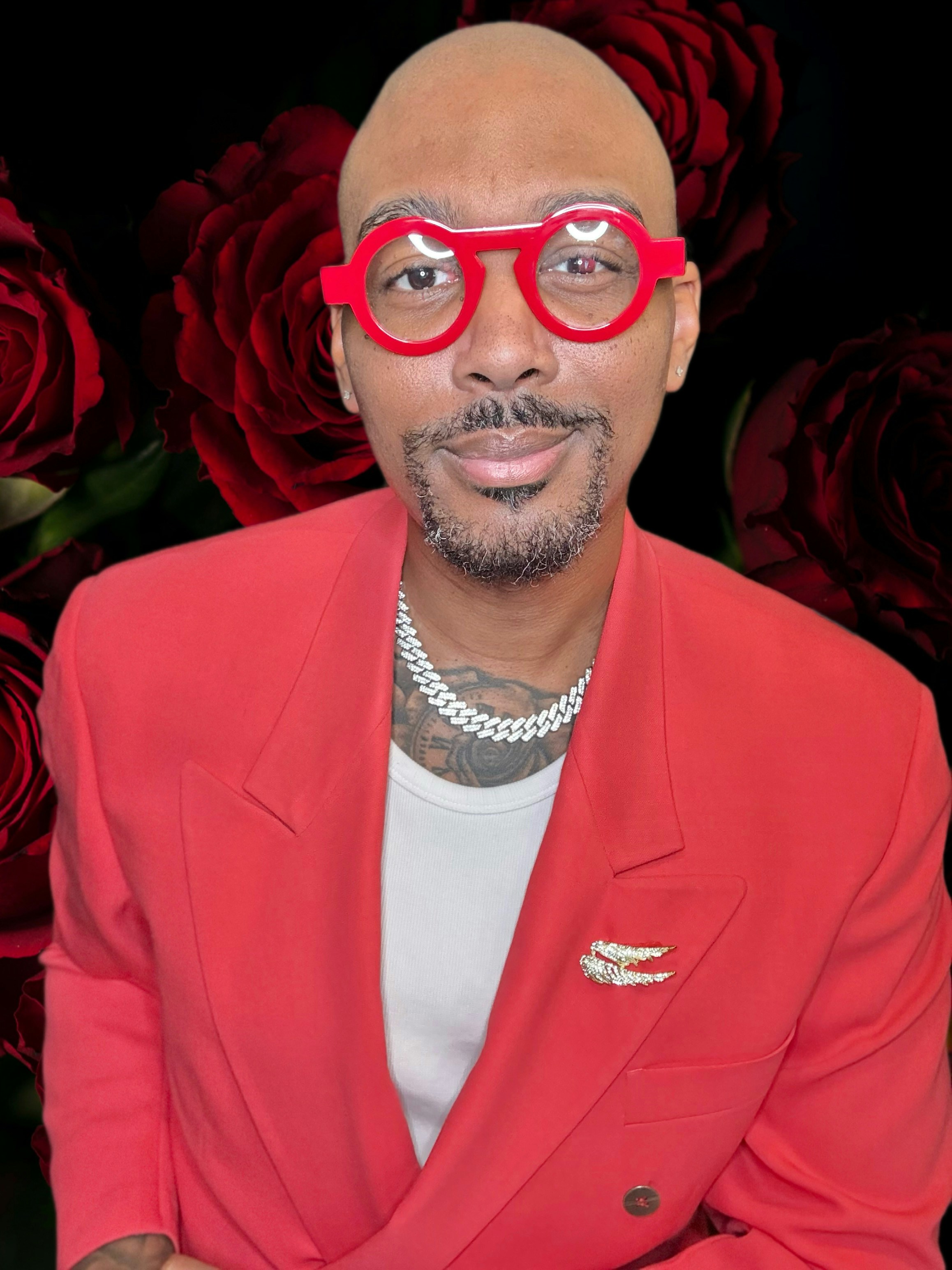 A man in a red blazer and white tank top wearing red glasses