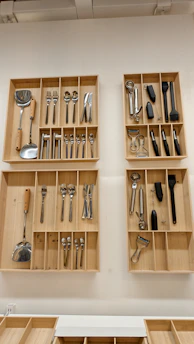 Four wooden drawer organizers mounted on a white wall containing various kitchen utensils