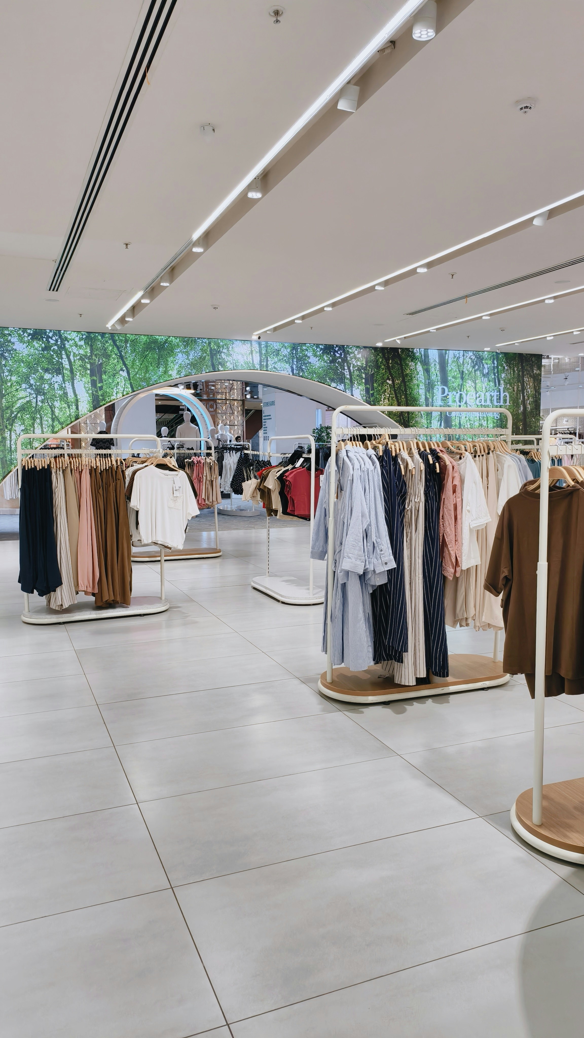 Clothing racks with shirts and trousers in a bright retail store with forest wallpaper