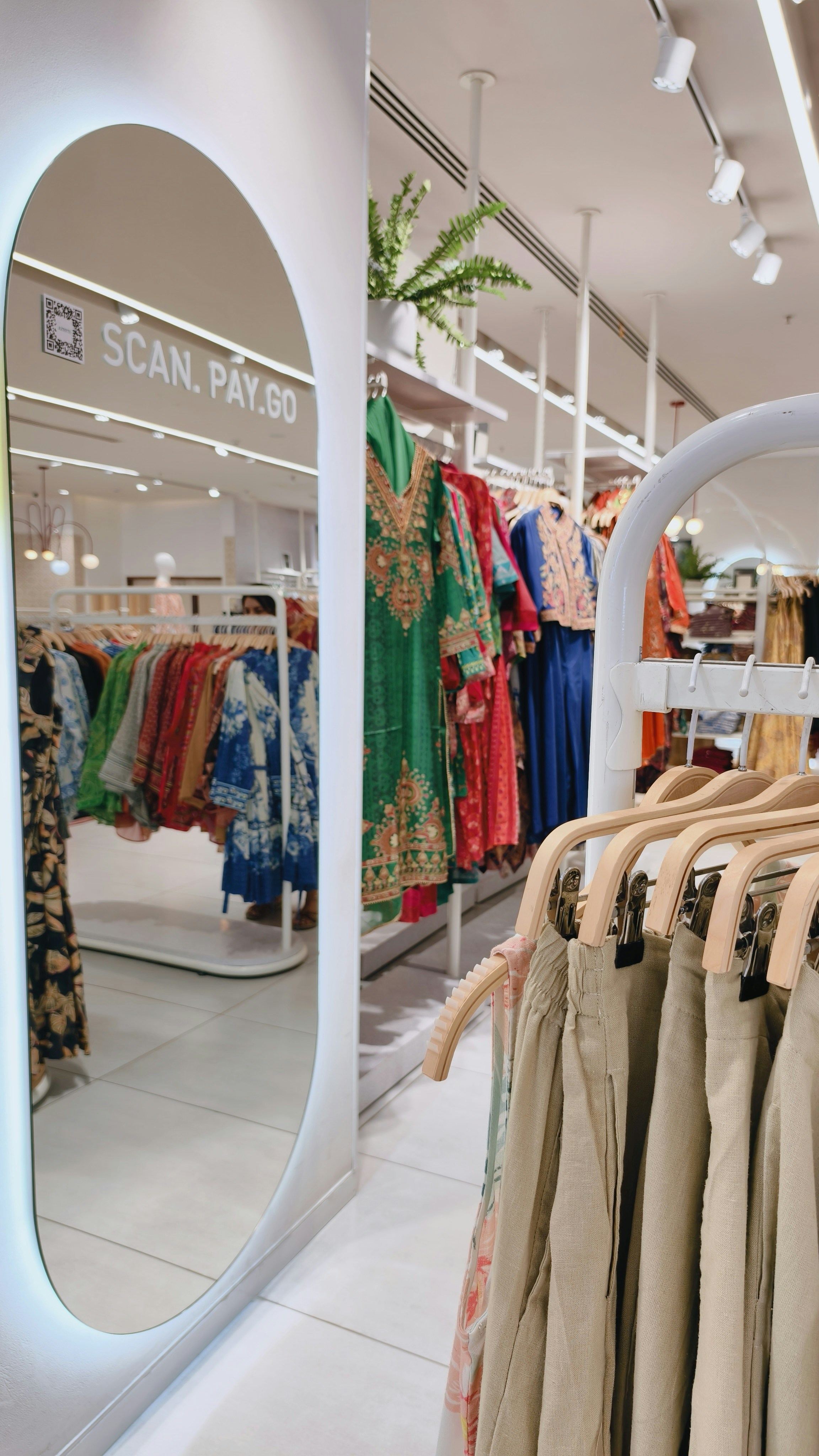 Clothing racks with colorful garments reflected in a large oval mirror in a store