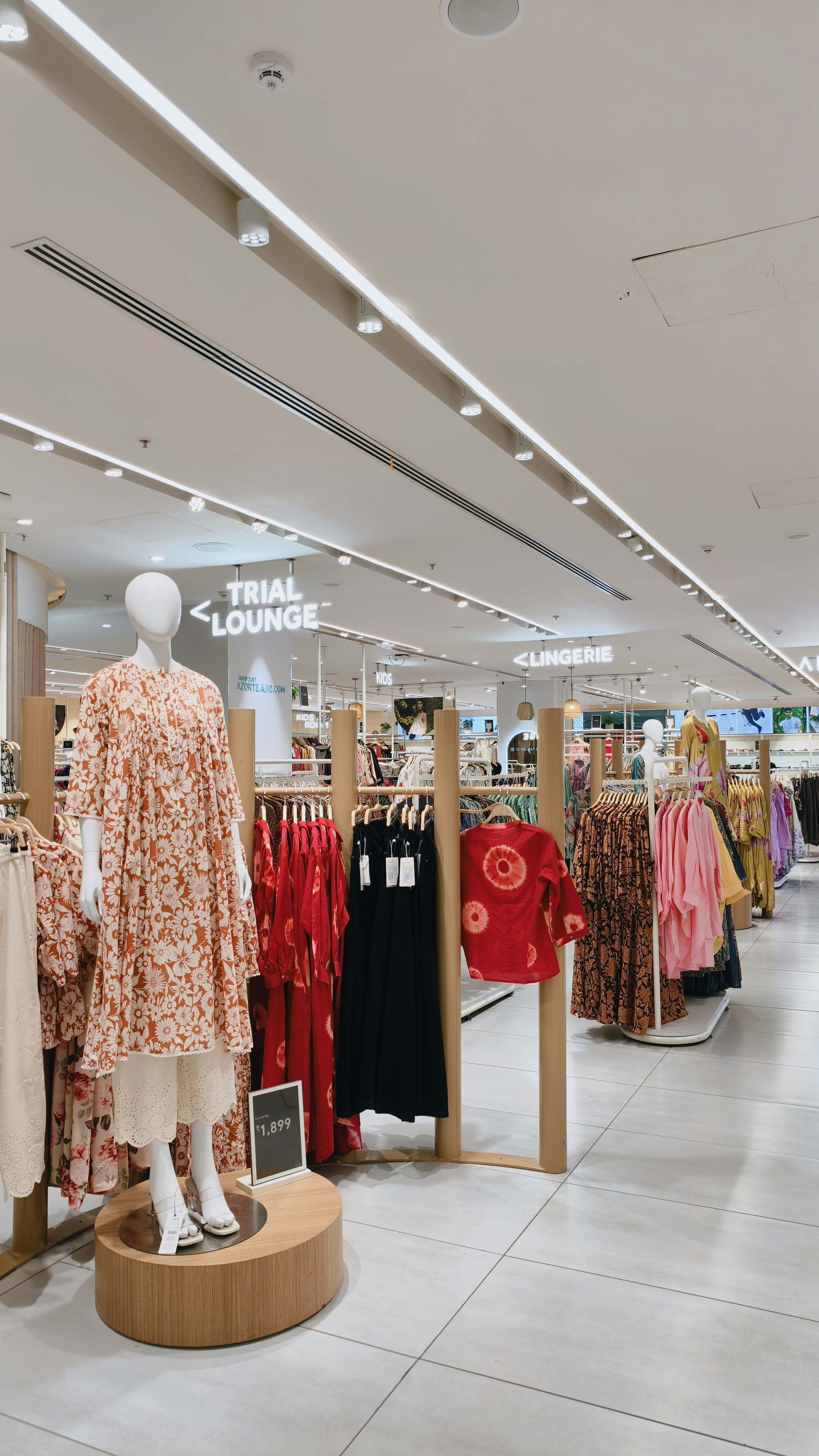 A mannequin wearing a floral dress in a clothing store with racks of apparel