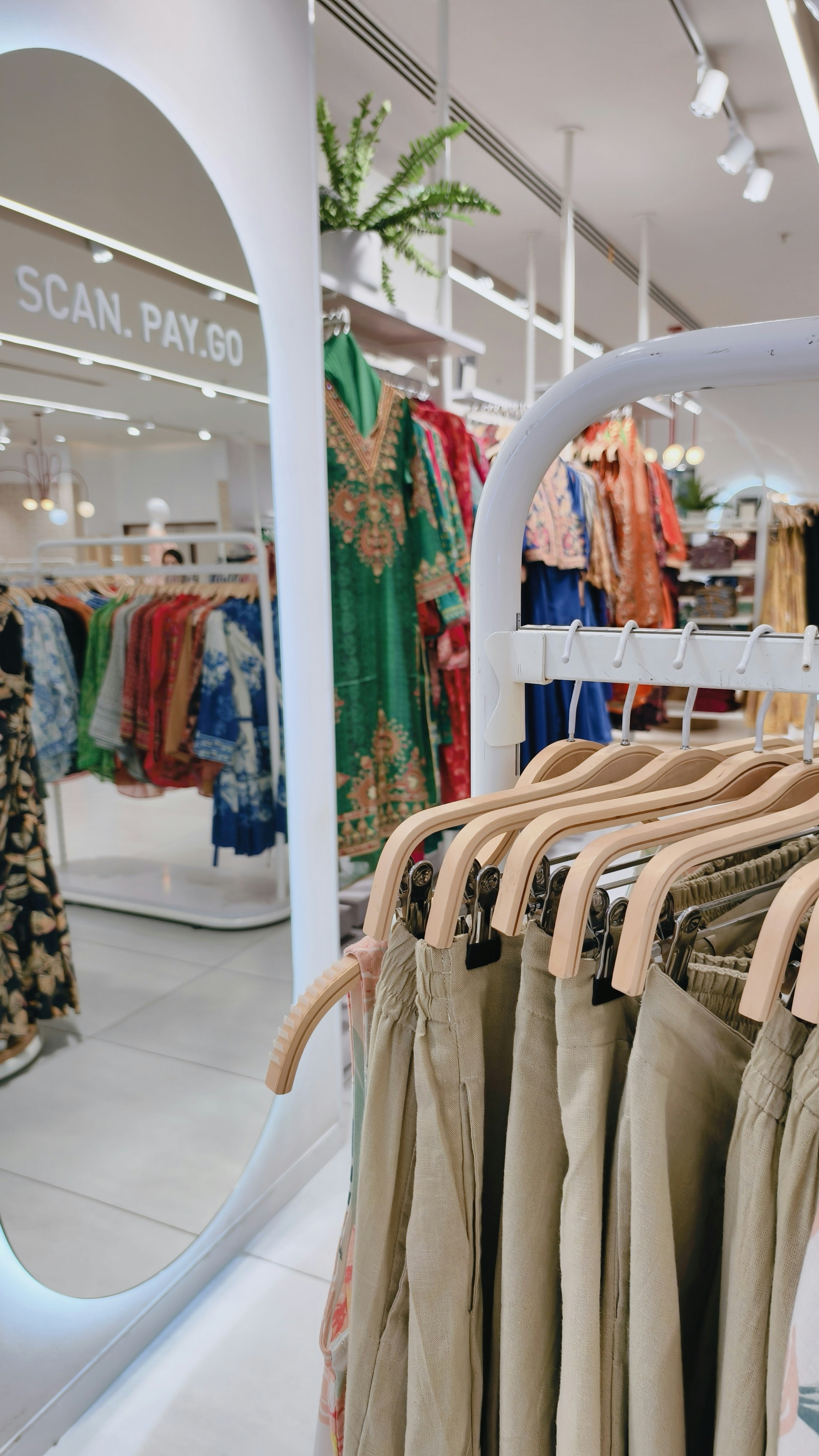 Beige trousers on wooden hangers in a clothing store with racks of colorful garments