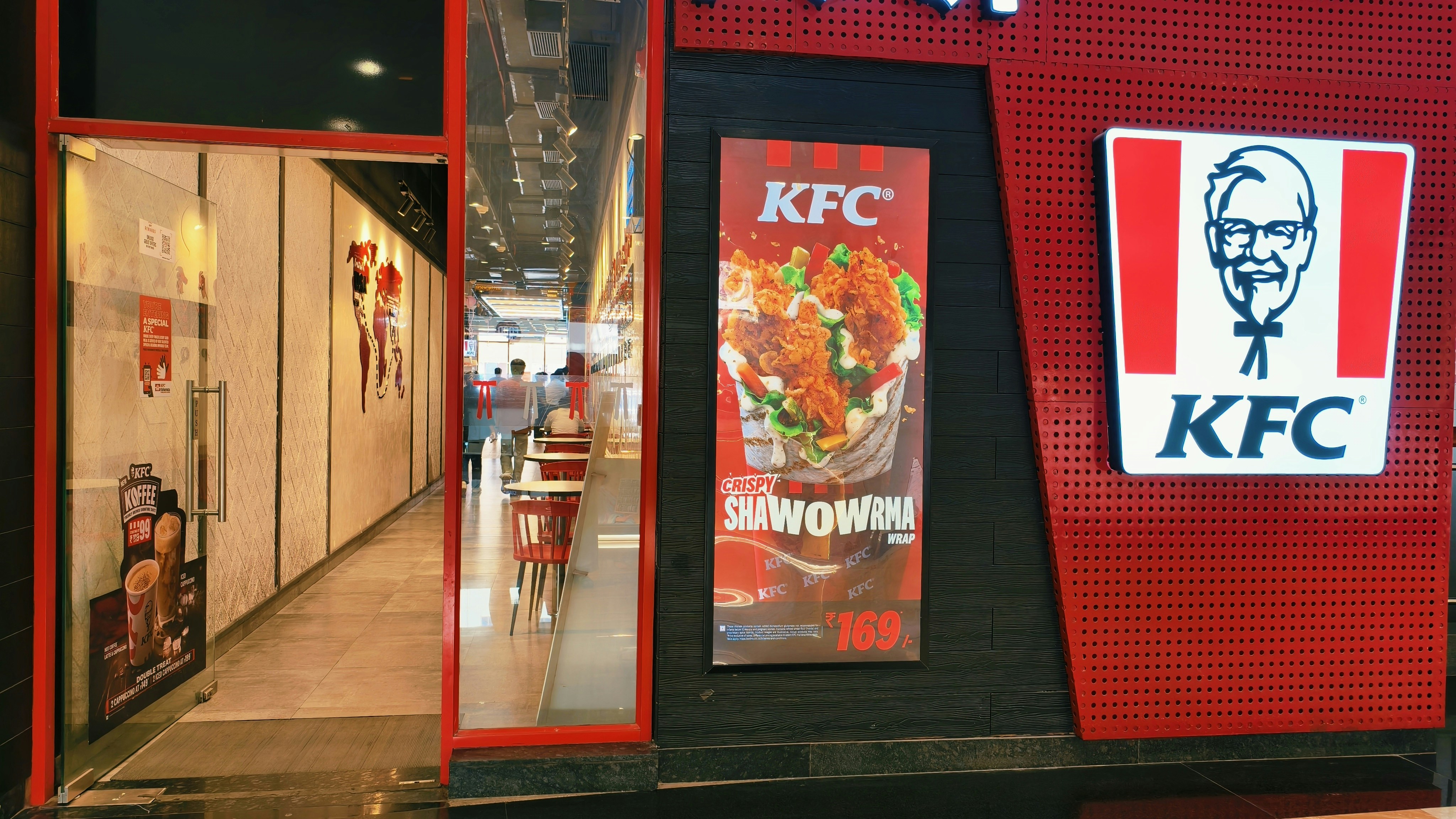 The exterior of a KFC restaurant with a large illuminated logo and menu poster