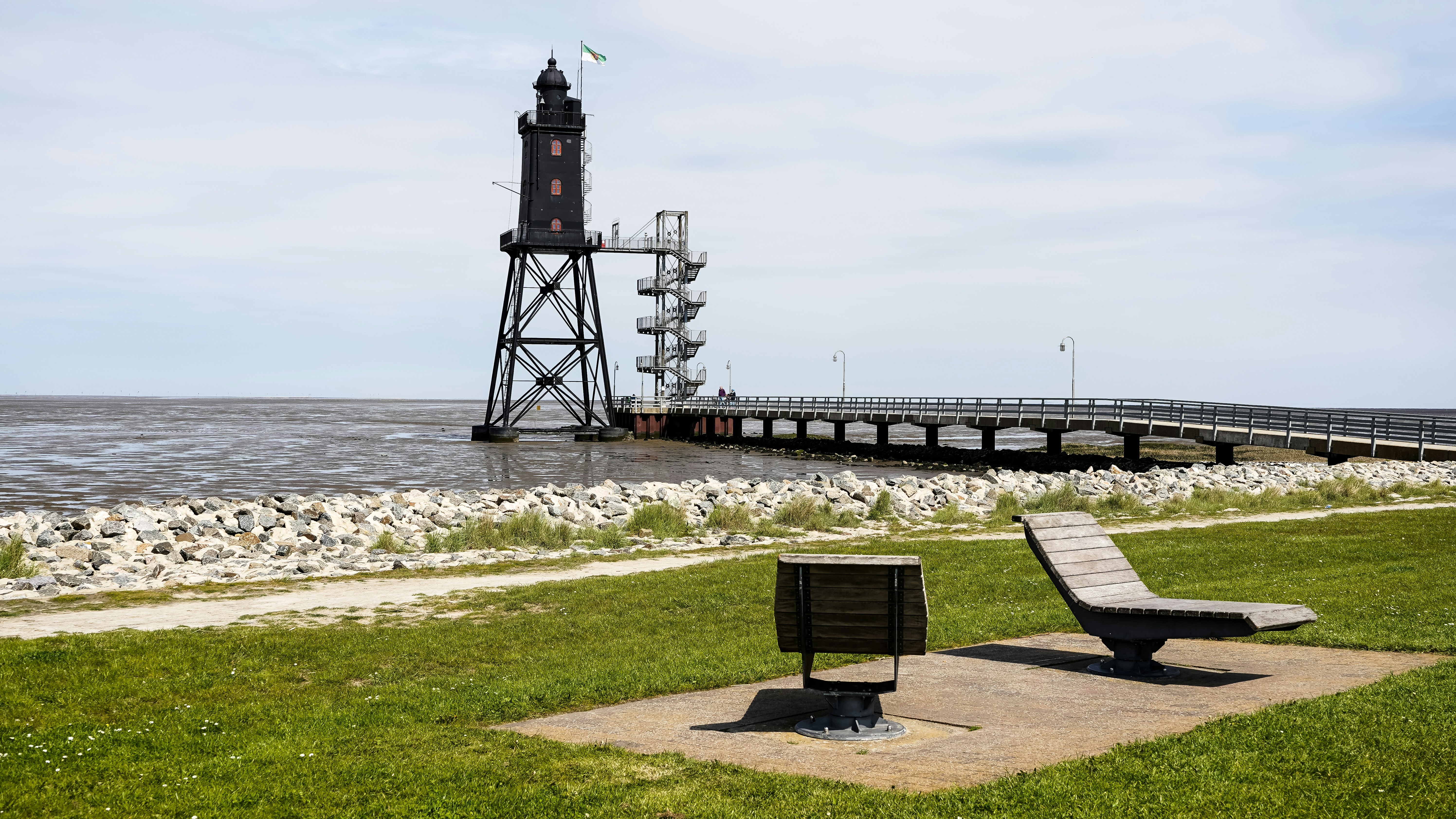 A black lighthouse on a metal frame with a pier extending into the water
