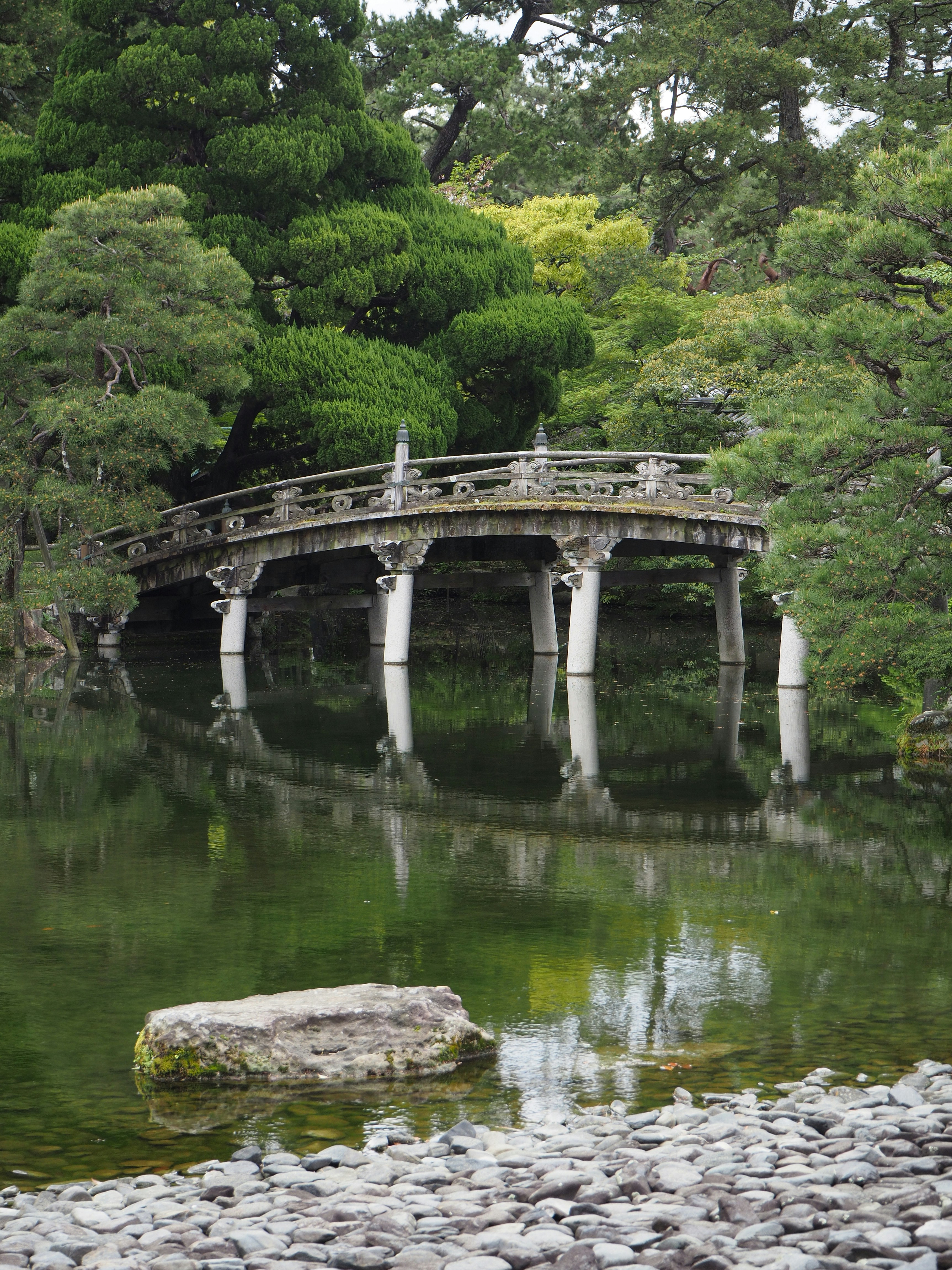 緑豊かな木々に囲む穏やかな池にかかるアーチ型の石橋
