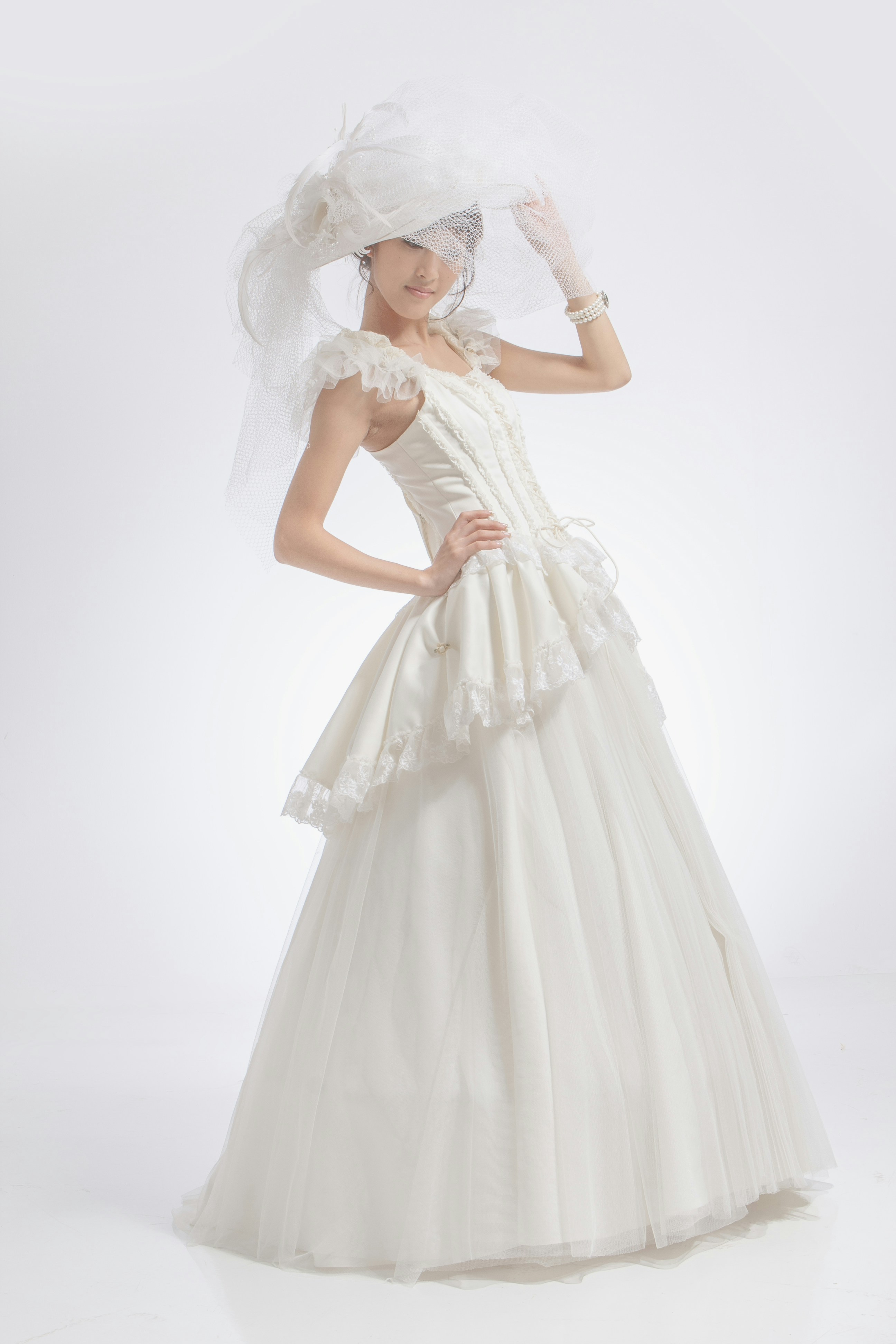 A woman in a white wedding dress and veil posing against a plain background
