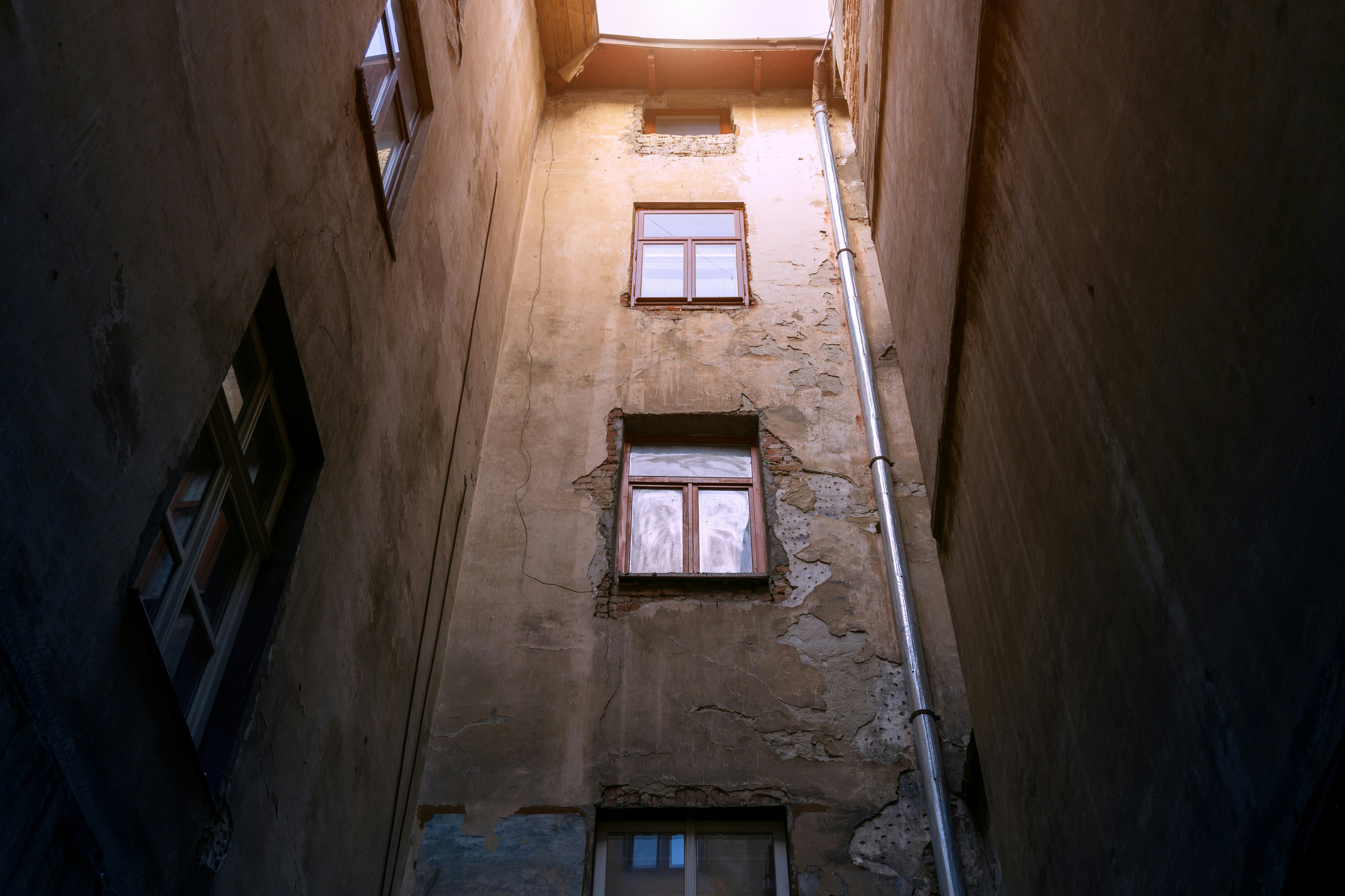 A narrow alleyway between weathered buildings with peeling plaster and windows