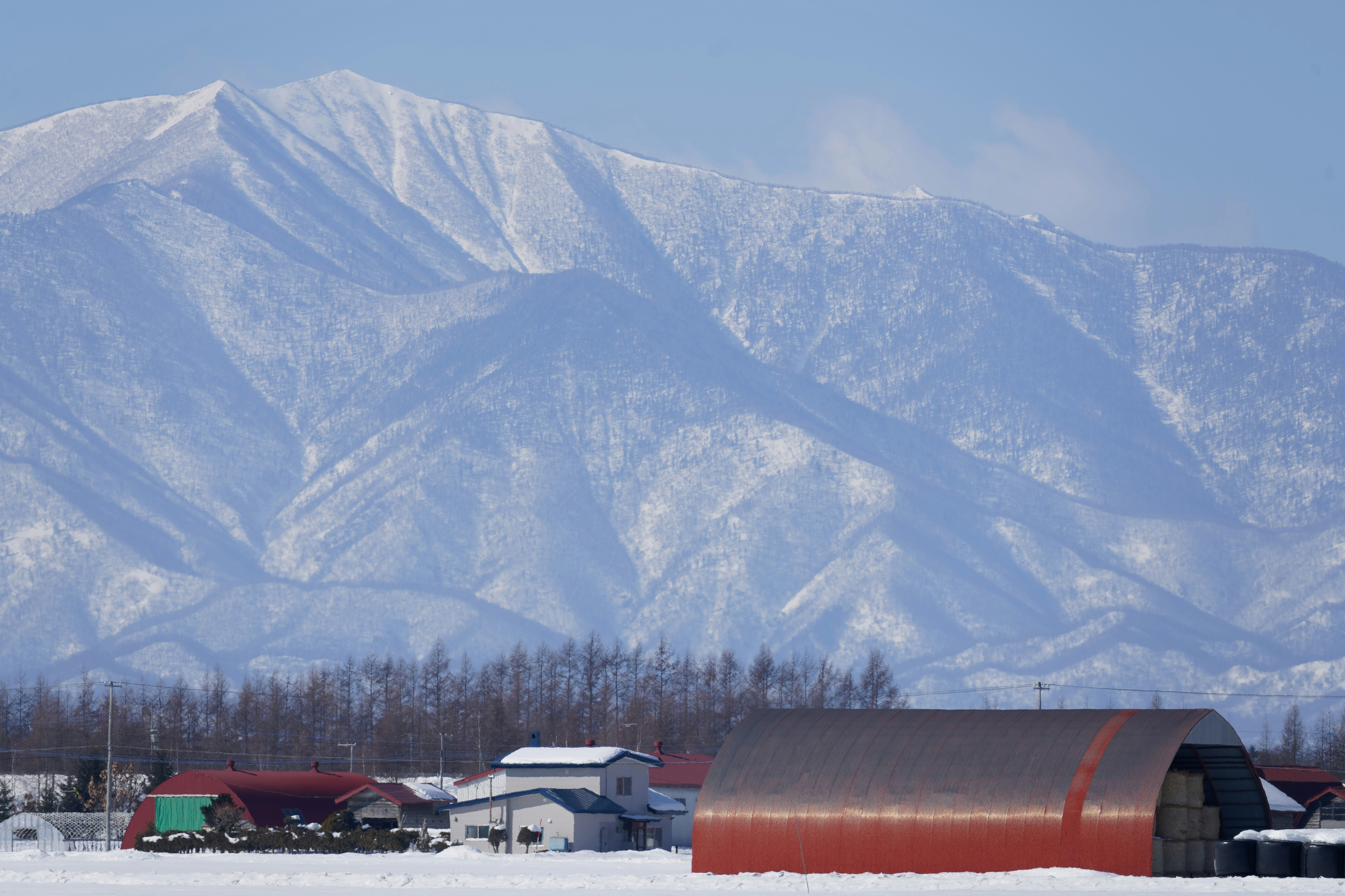 Um celeiro em arco vermelho e casas em um campo nevado abaixo das montanhas cobertas de neve
