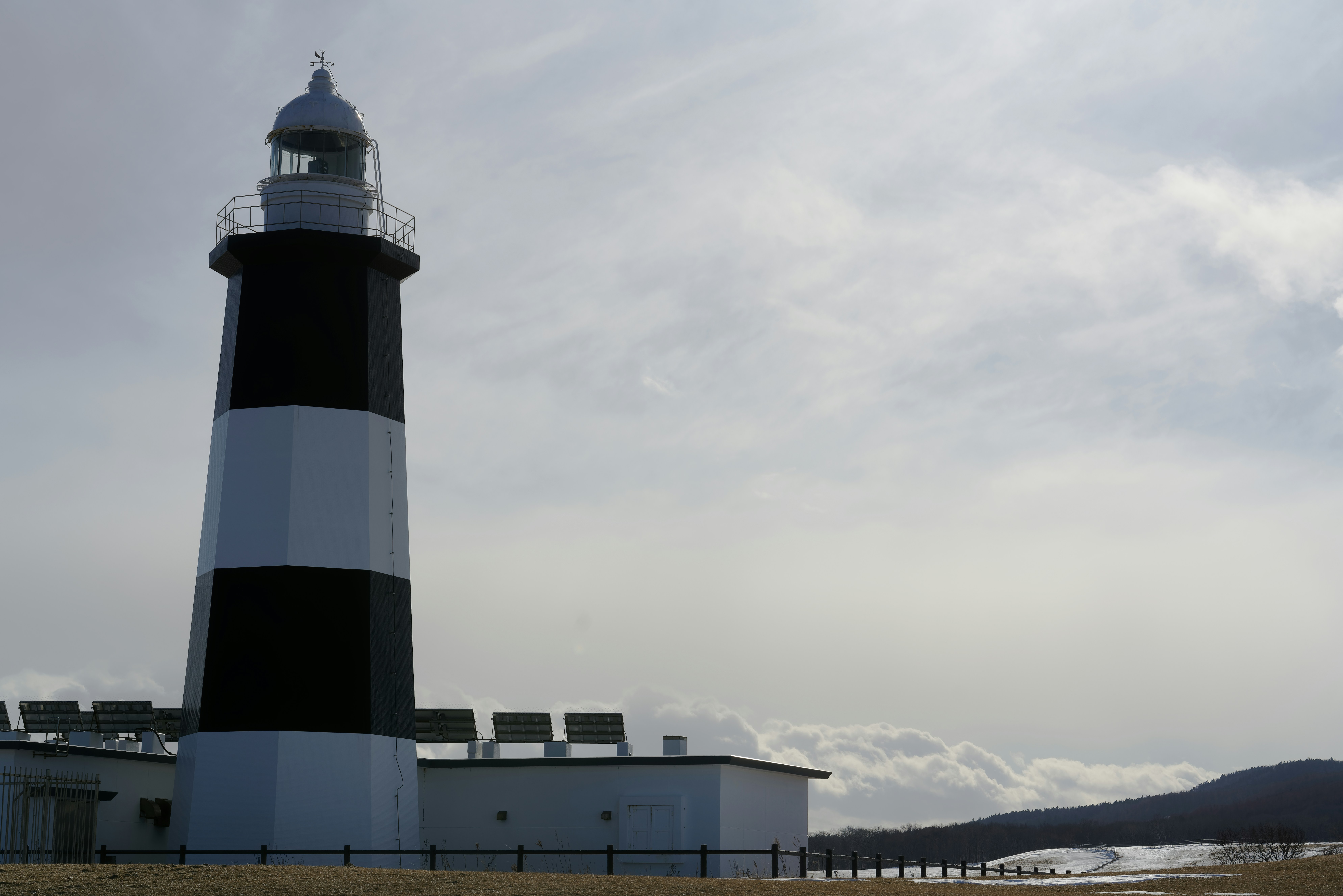 Um farol listrado em preto e branco em uma paisagem nevada sob um céu nublado