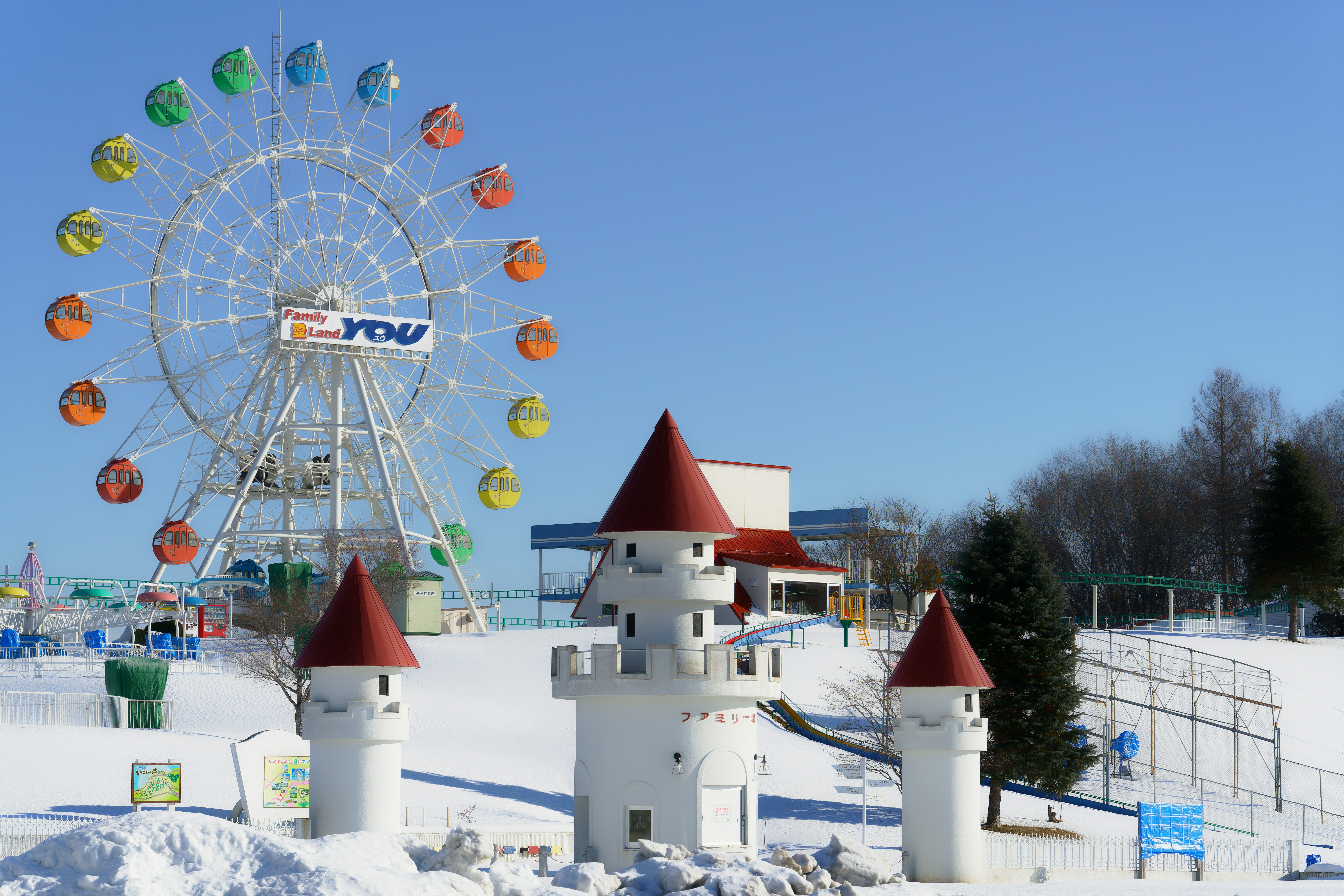 Uma roda-gigante colorida e um castelo branco se erguem em um parque de diversões coberto de neve