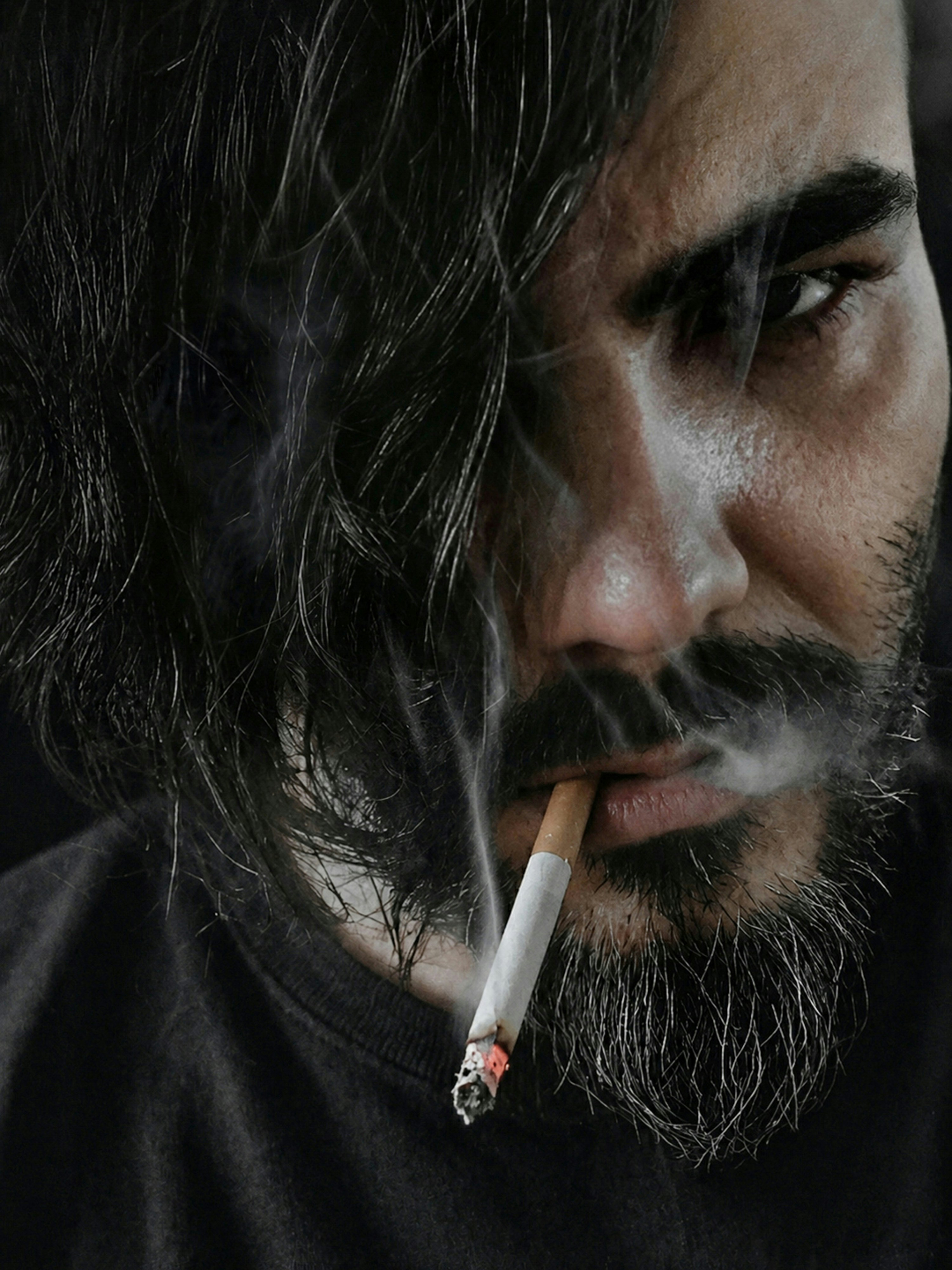 A man with dark hair and a beard smoking a cigarette