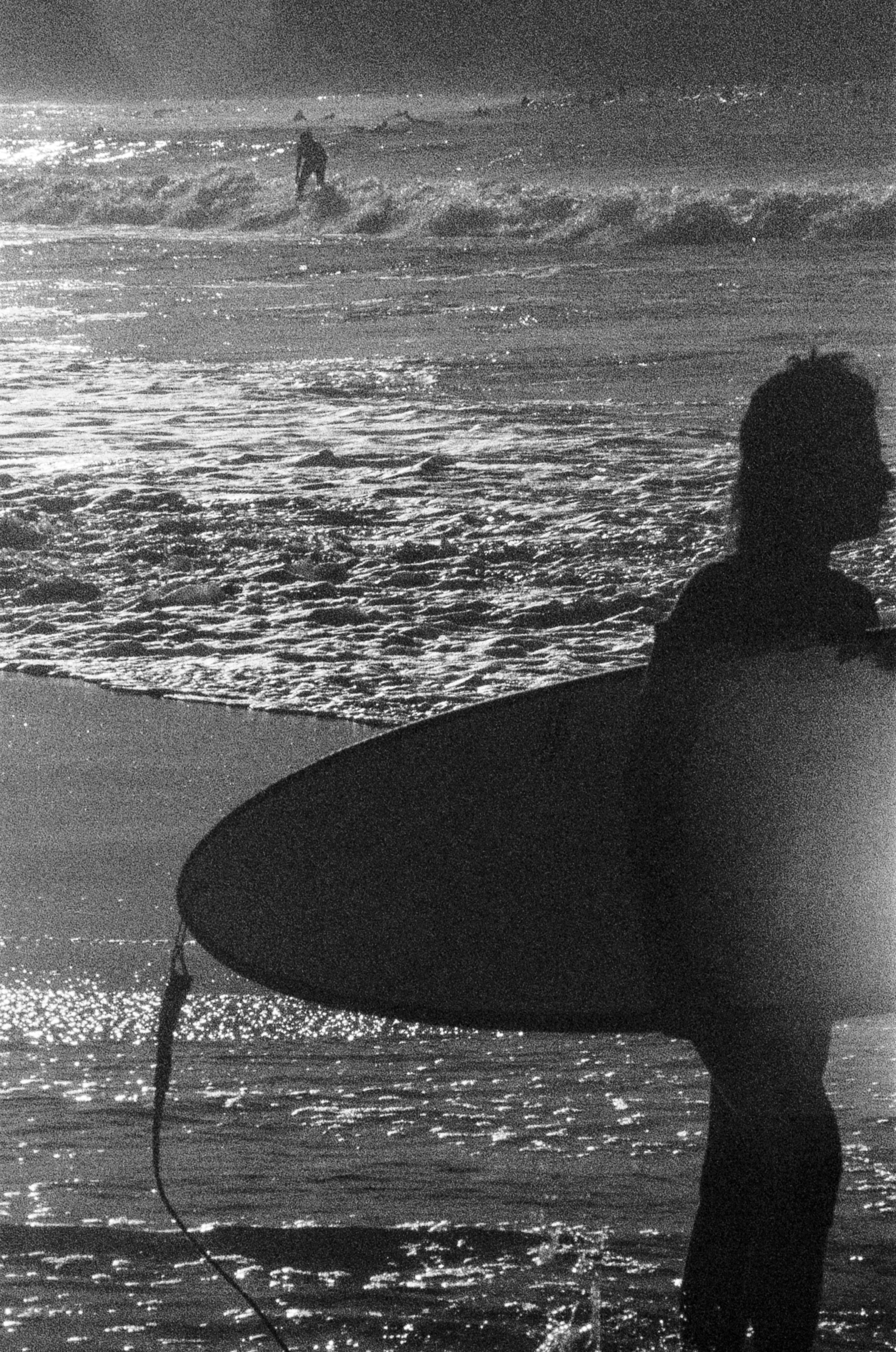 A person in silhouette holding a surfboard on a beach with waves