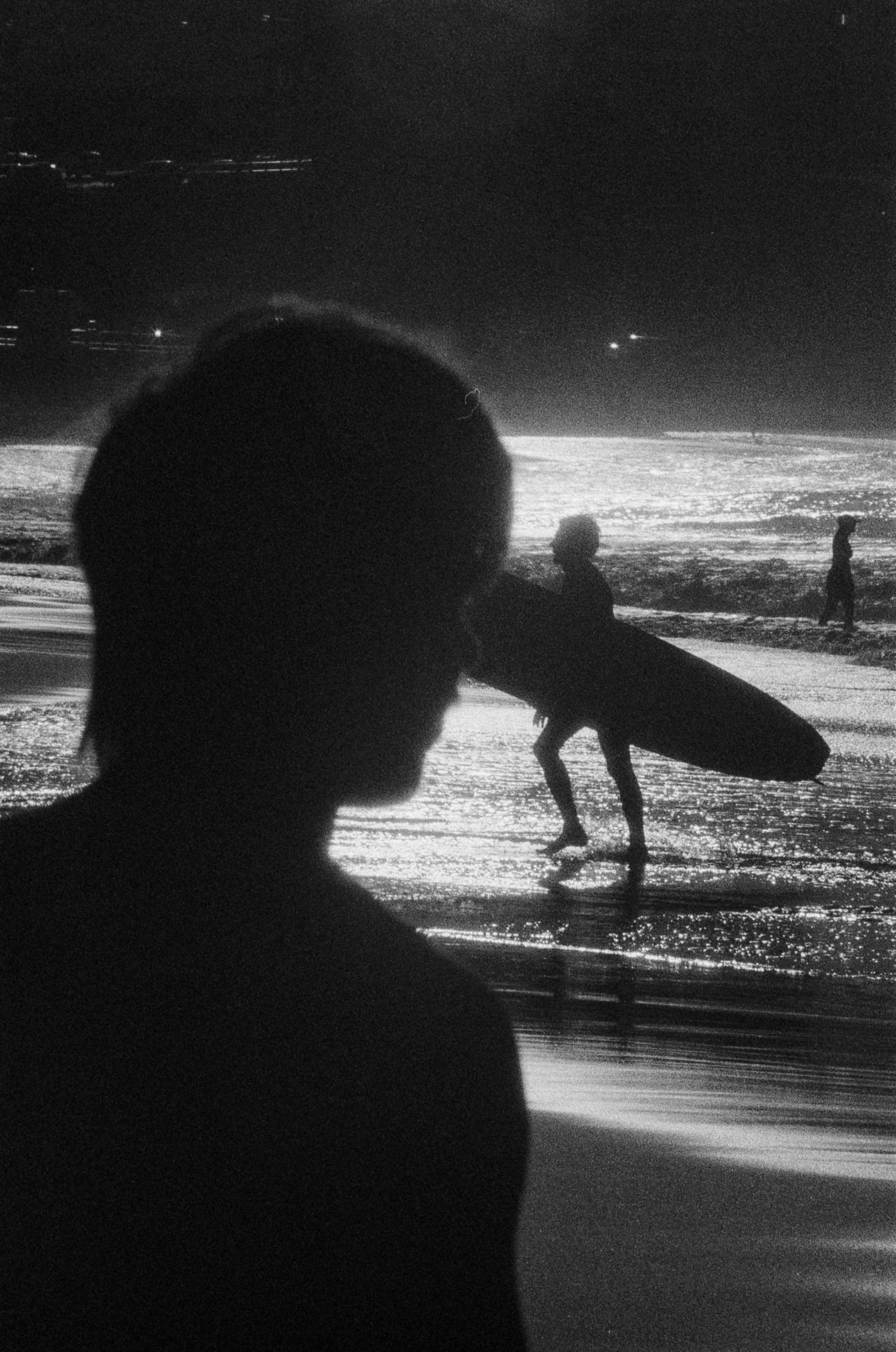 Una persona en silueta llevando una tabla de surf en una playa de noche