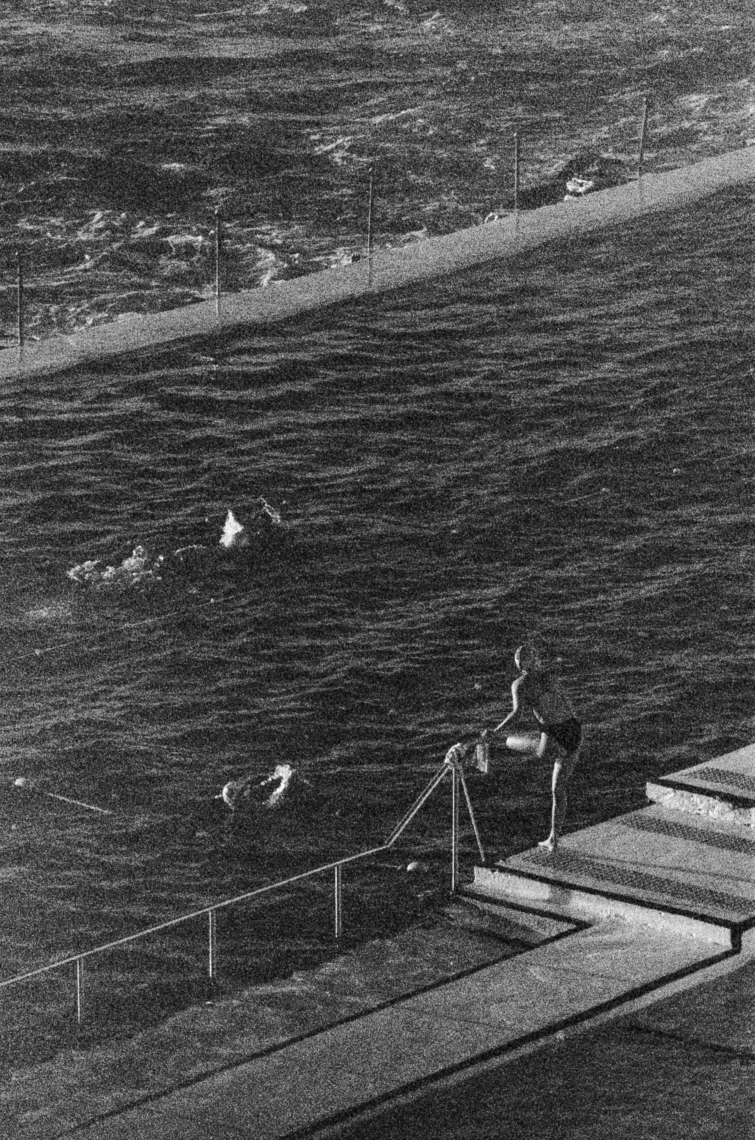 Una persona en bañador entrando en una piscina junto a un océano agitado