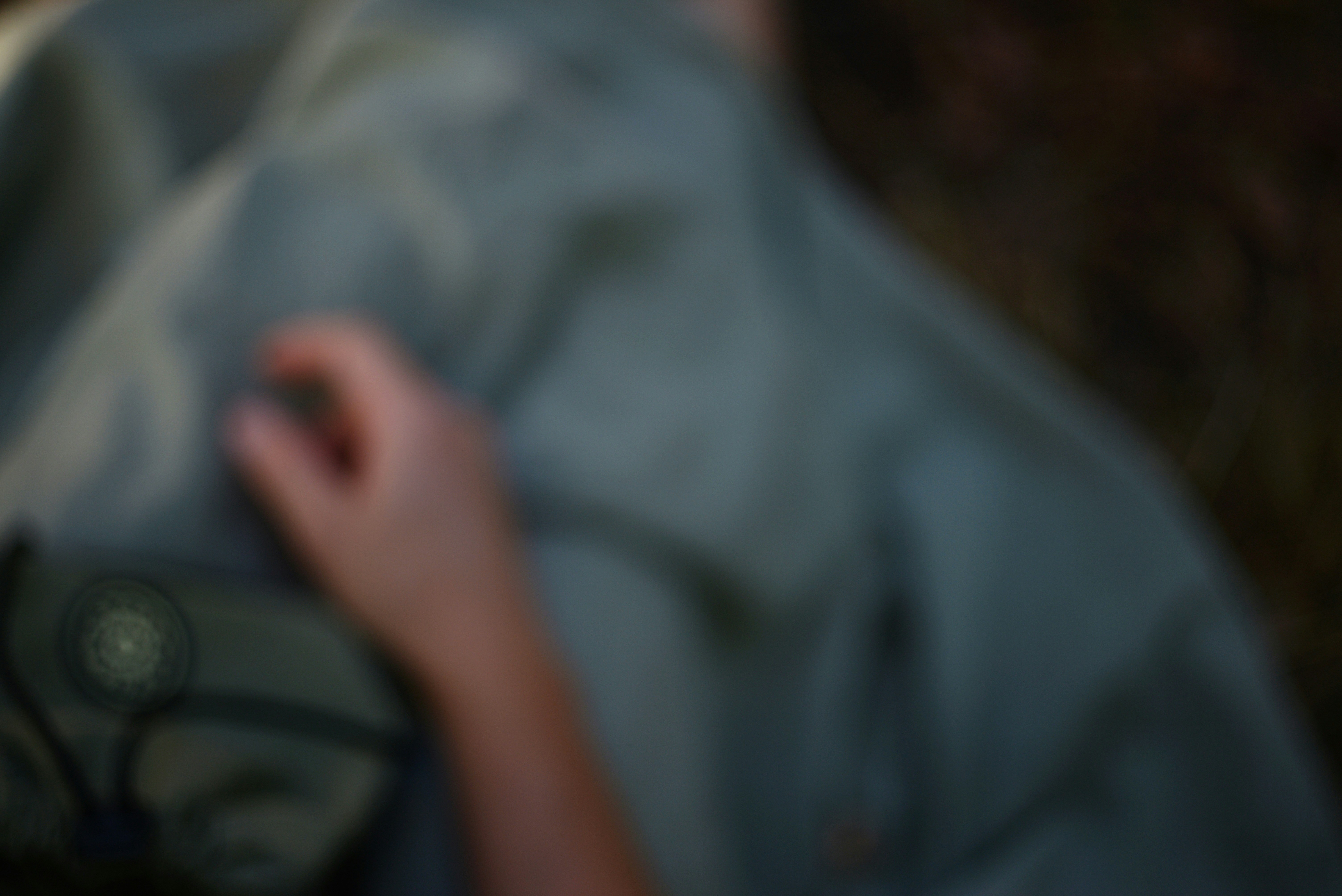 A blurred hand resting on a grey fabric surface with a small circular emblem