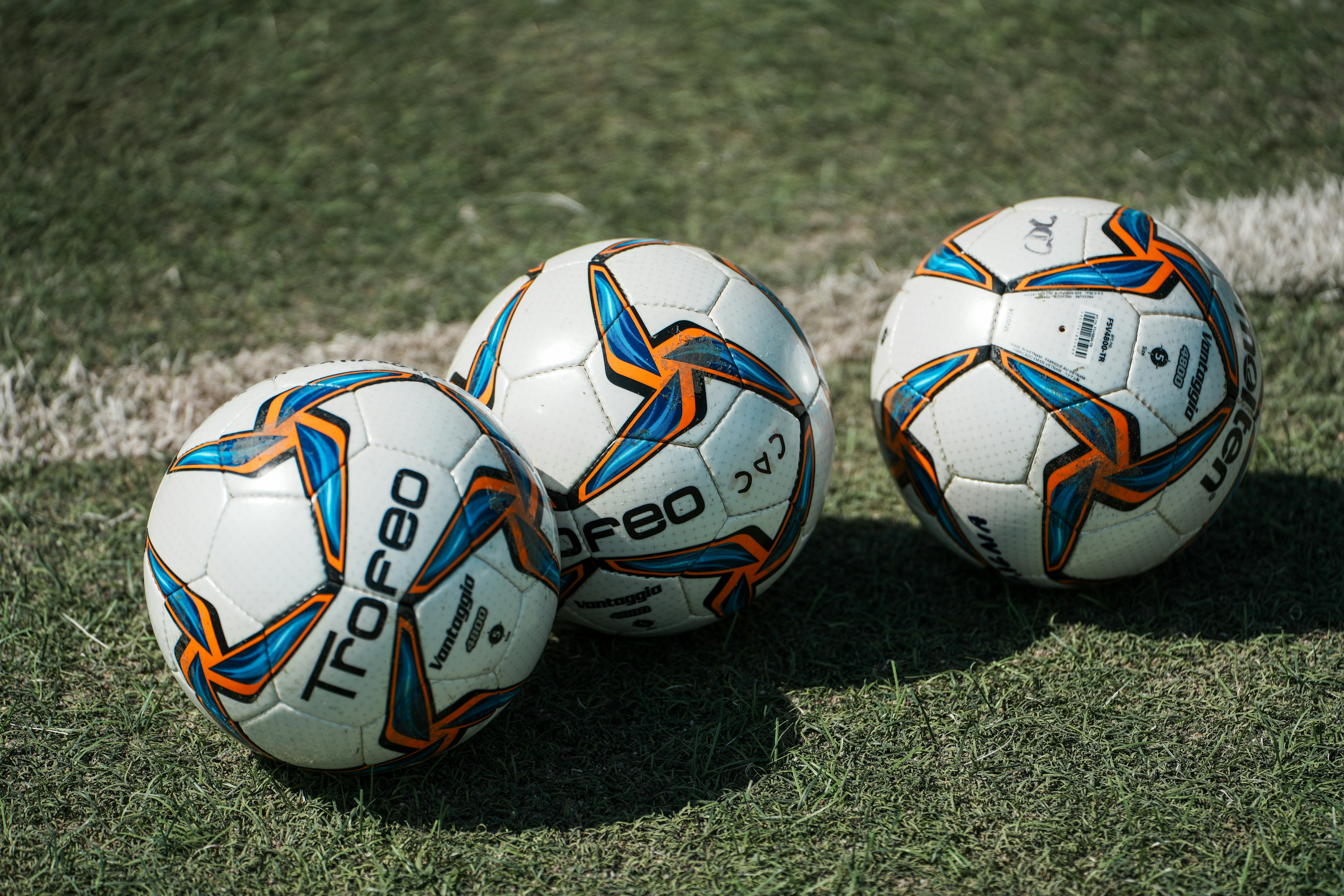 Three white soccer balls with blue and orange patterns on a grass field