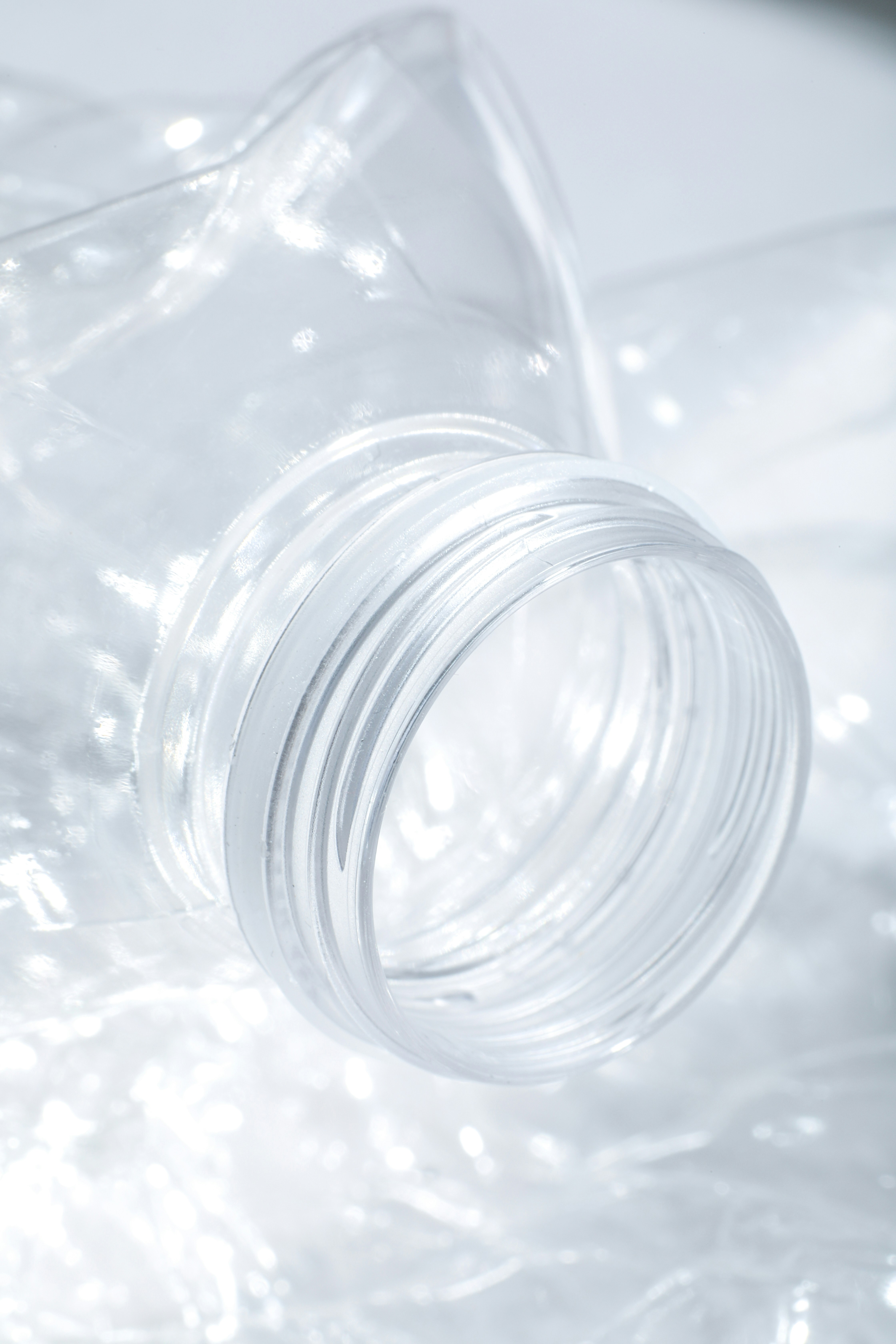 The threaded neck of a clear plastic bottle against a crinkled surface