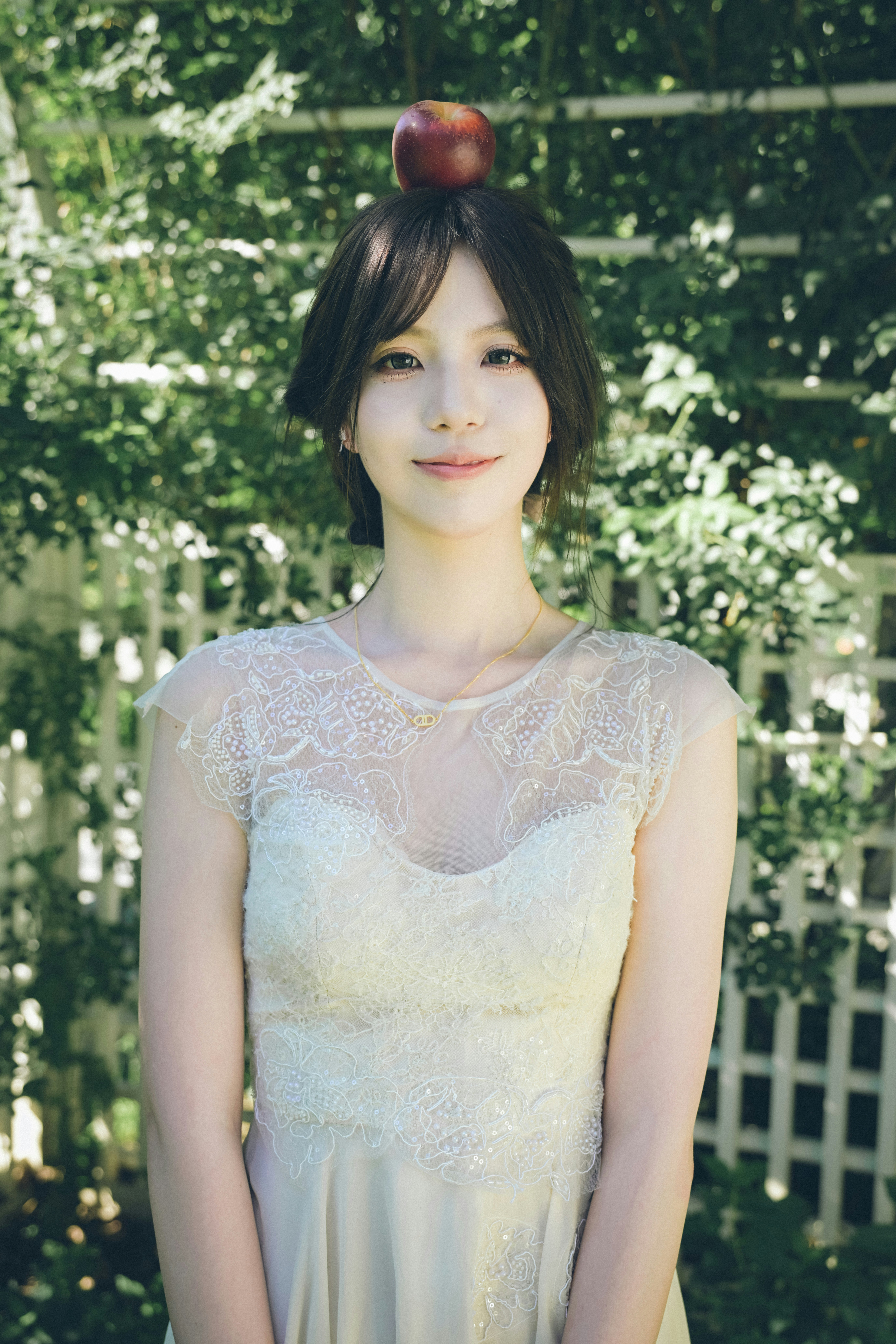 A woman in a white lace dress with an apple balanced on her head