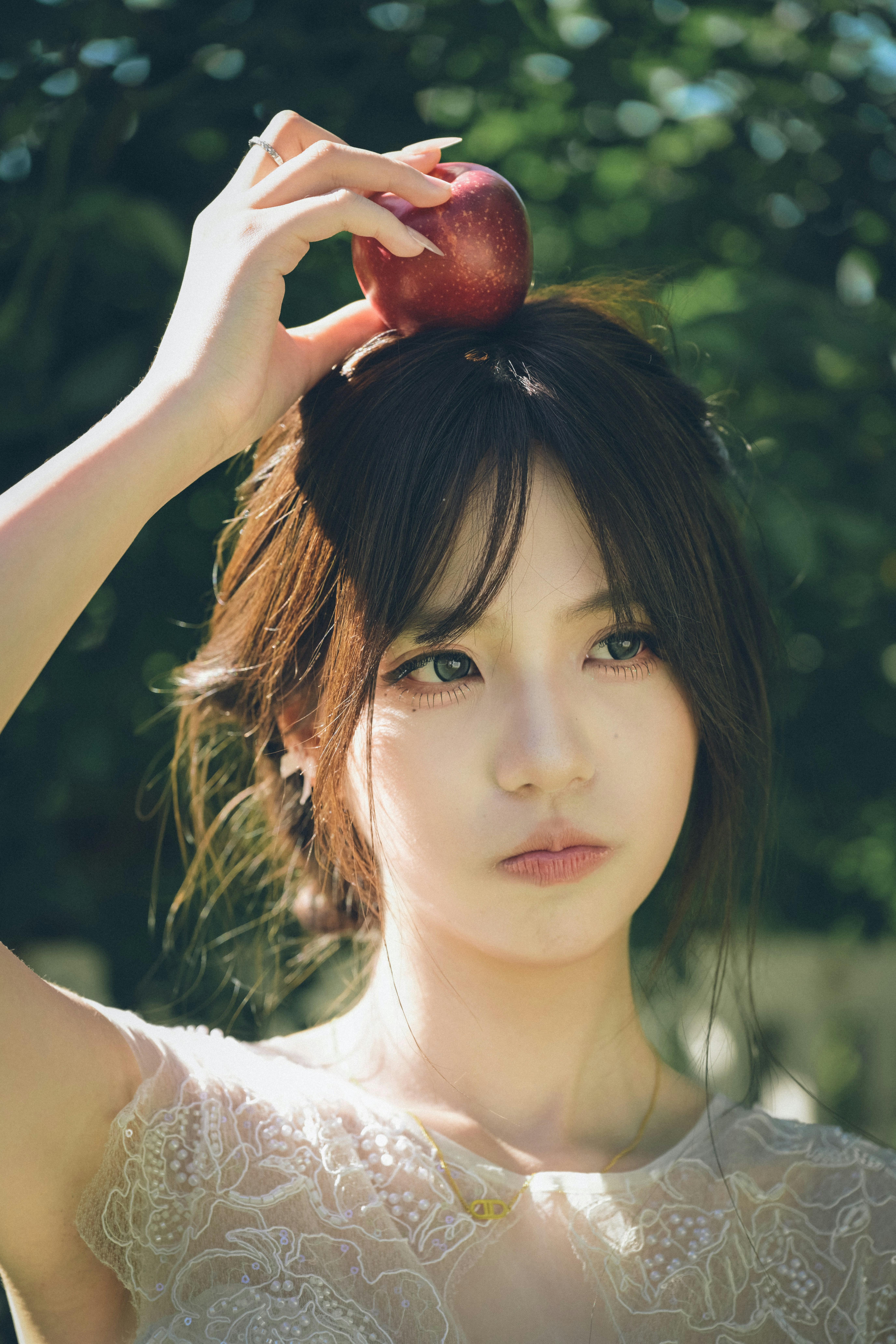 A woman balancing a red apple on her head in a sunlit garden