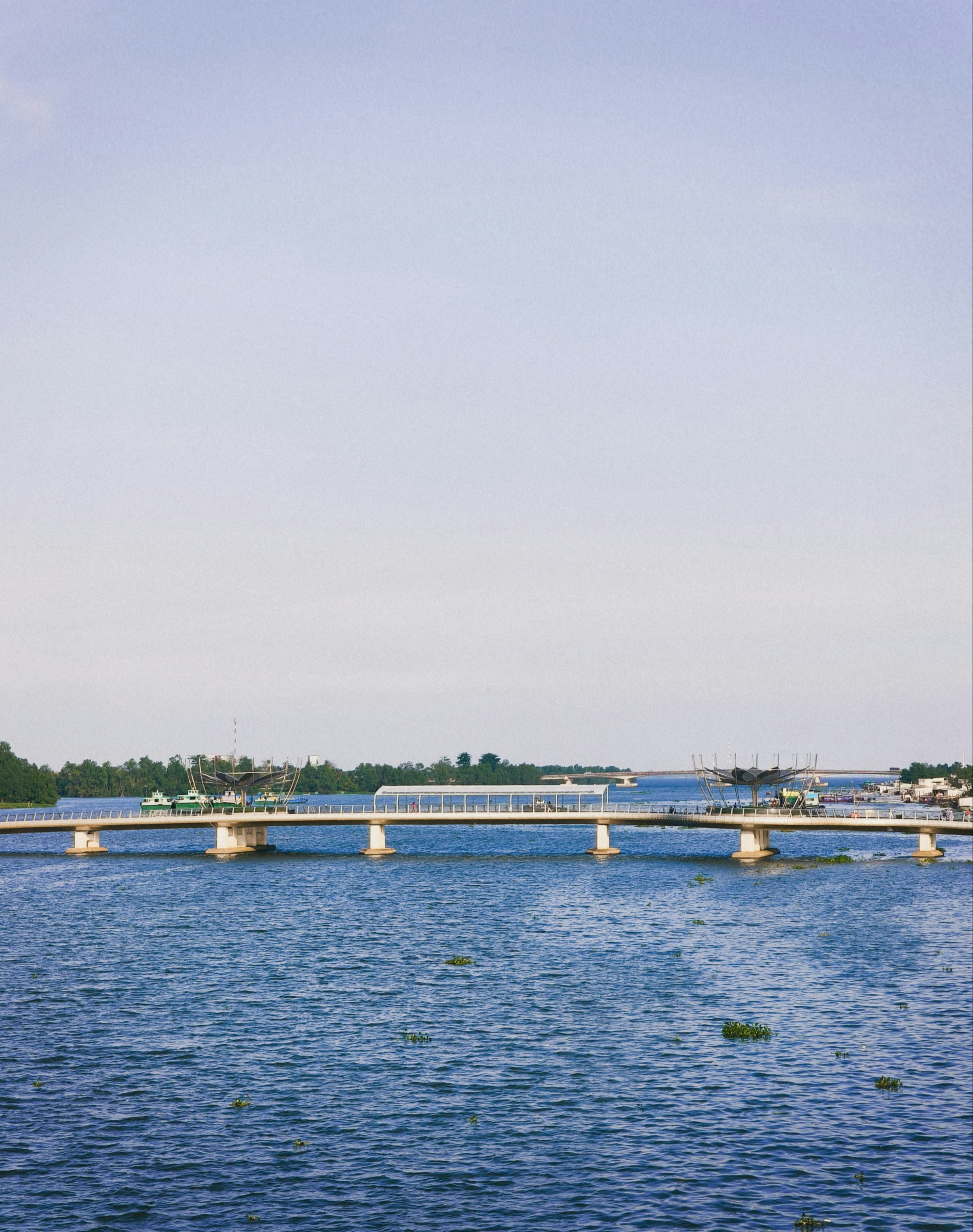 A long pedestrian bridge spanning a wide river under a clear blue sky