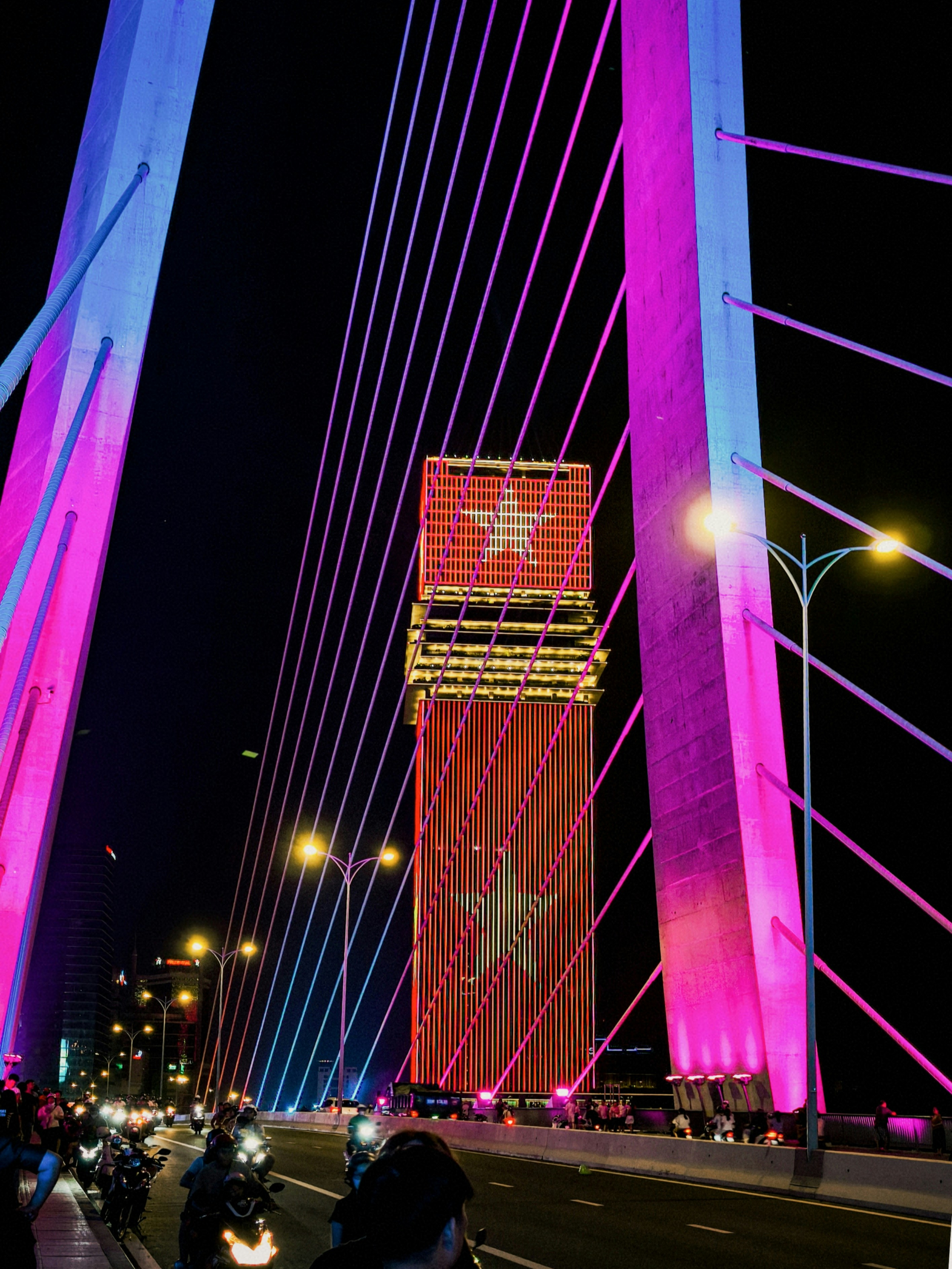 A cable-stayed bridge with pink lights and a tall building with star patterns
