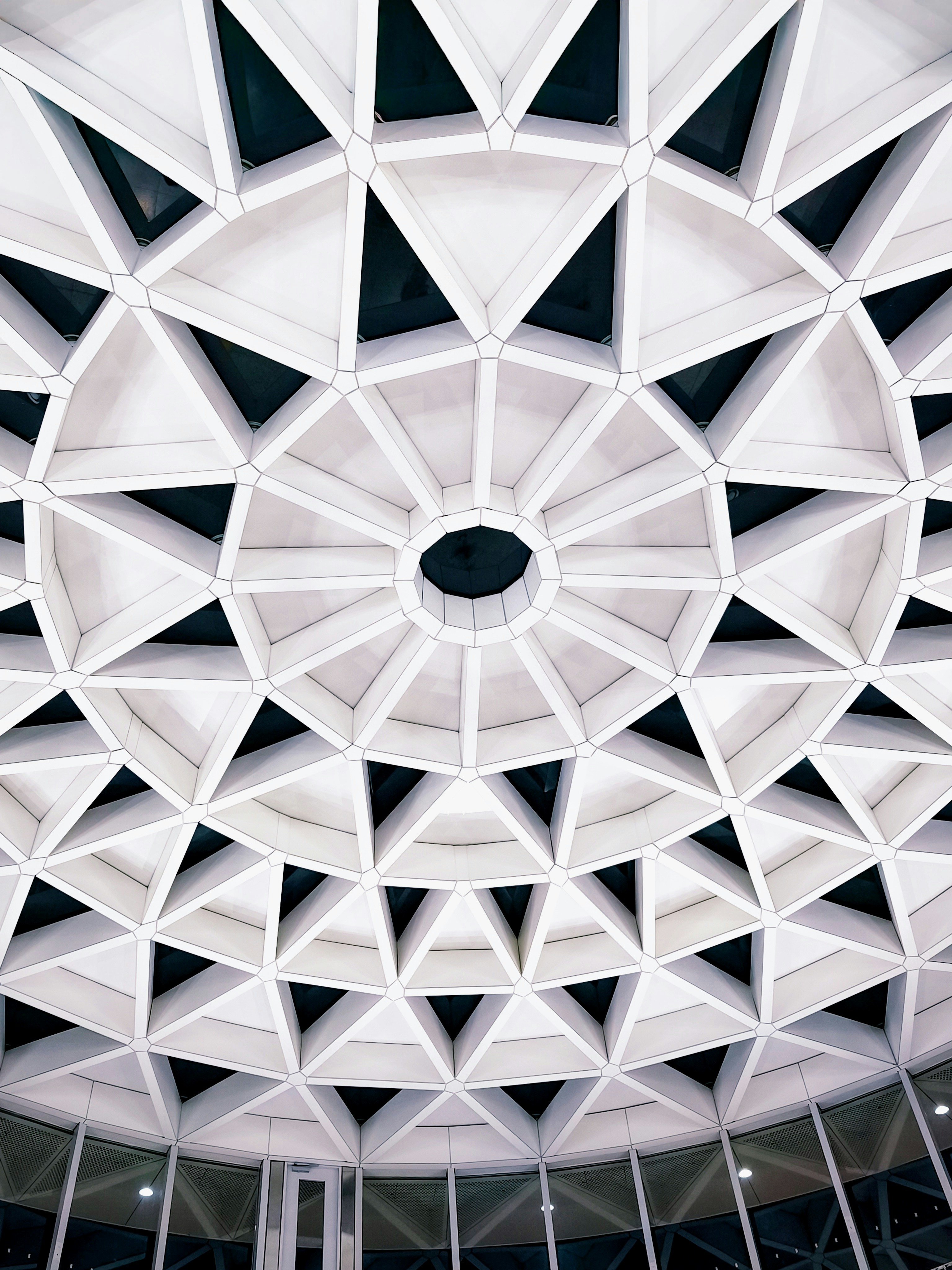 A white geometric ceiling with a repeating triangular pattern and a central circular opening