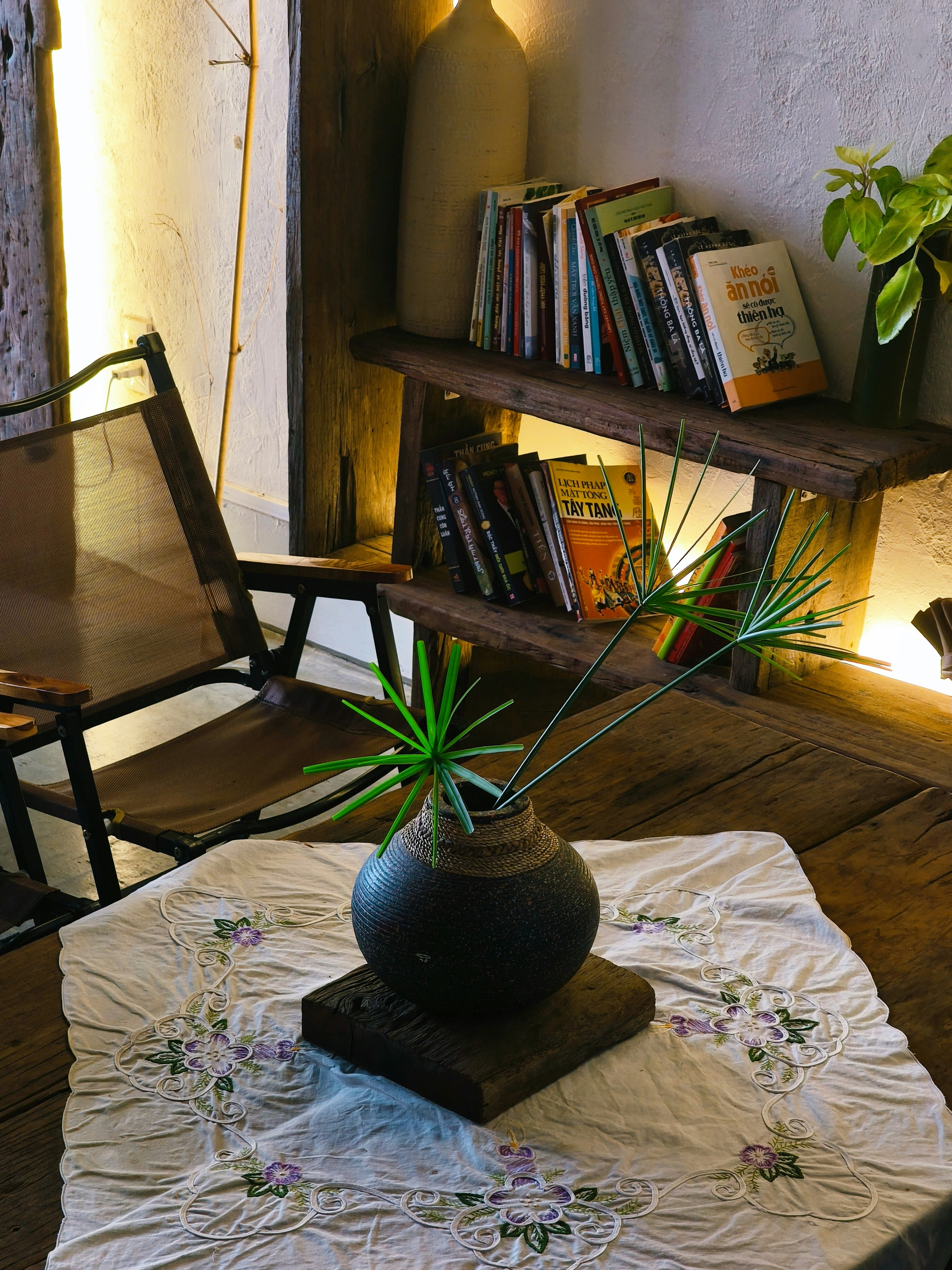 A dark ceramic vase with green papyrus stems on a white embroidered cloth