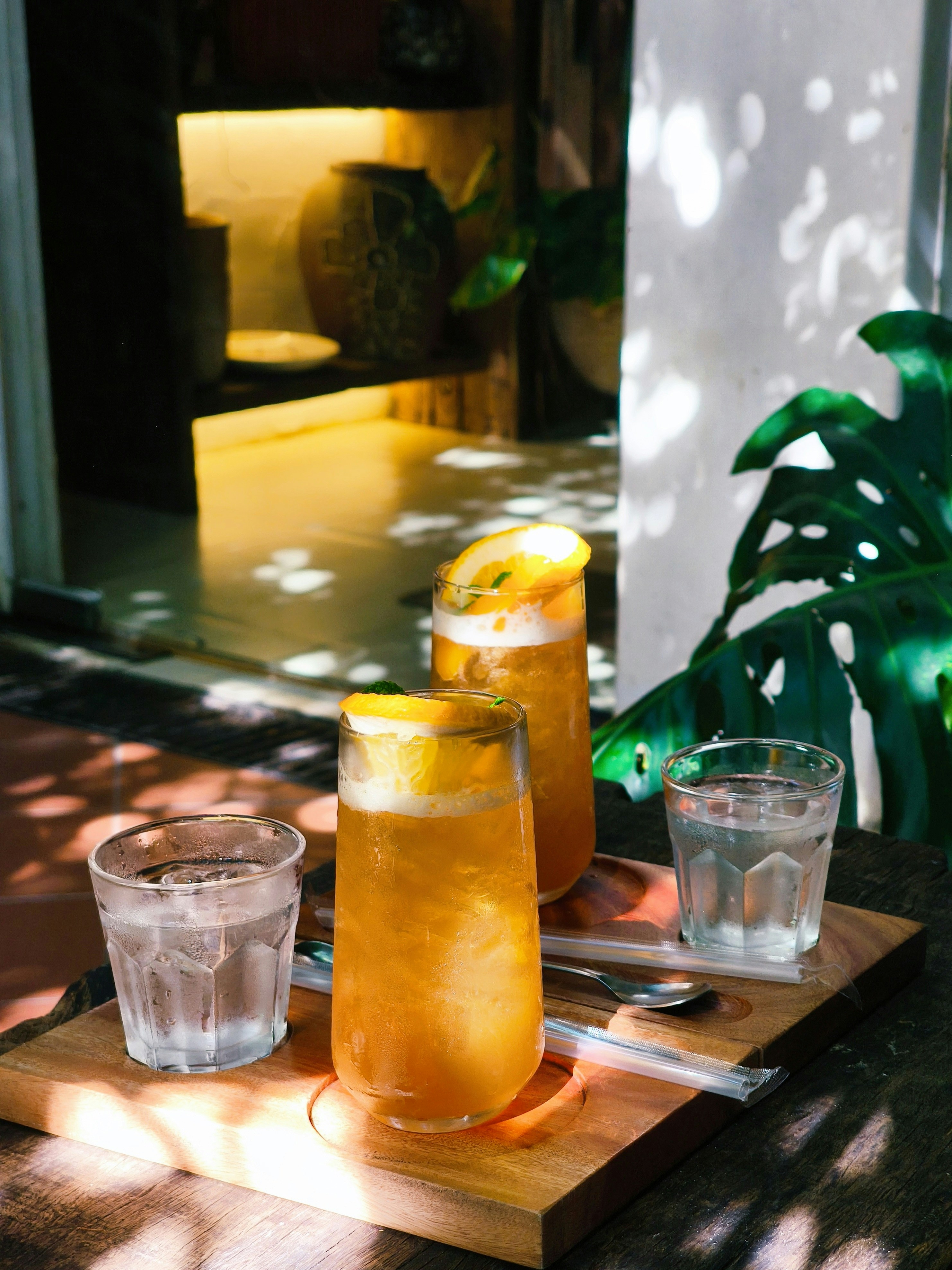 Two tall glasses of orange iced tea with water glasses on a wooden tray