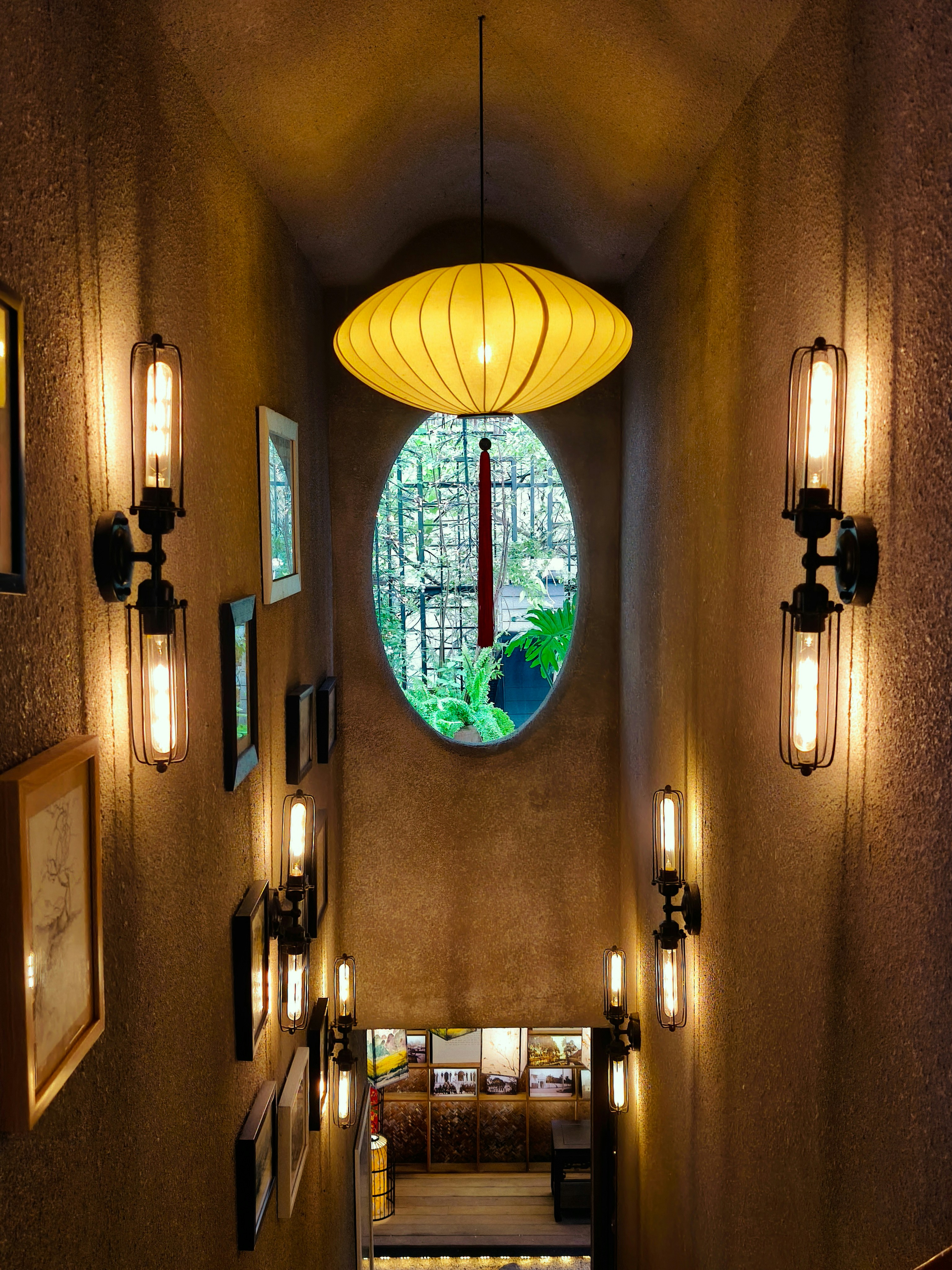 A narrow staircase with warm wall lamps and a yellow paper lantern