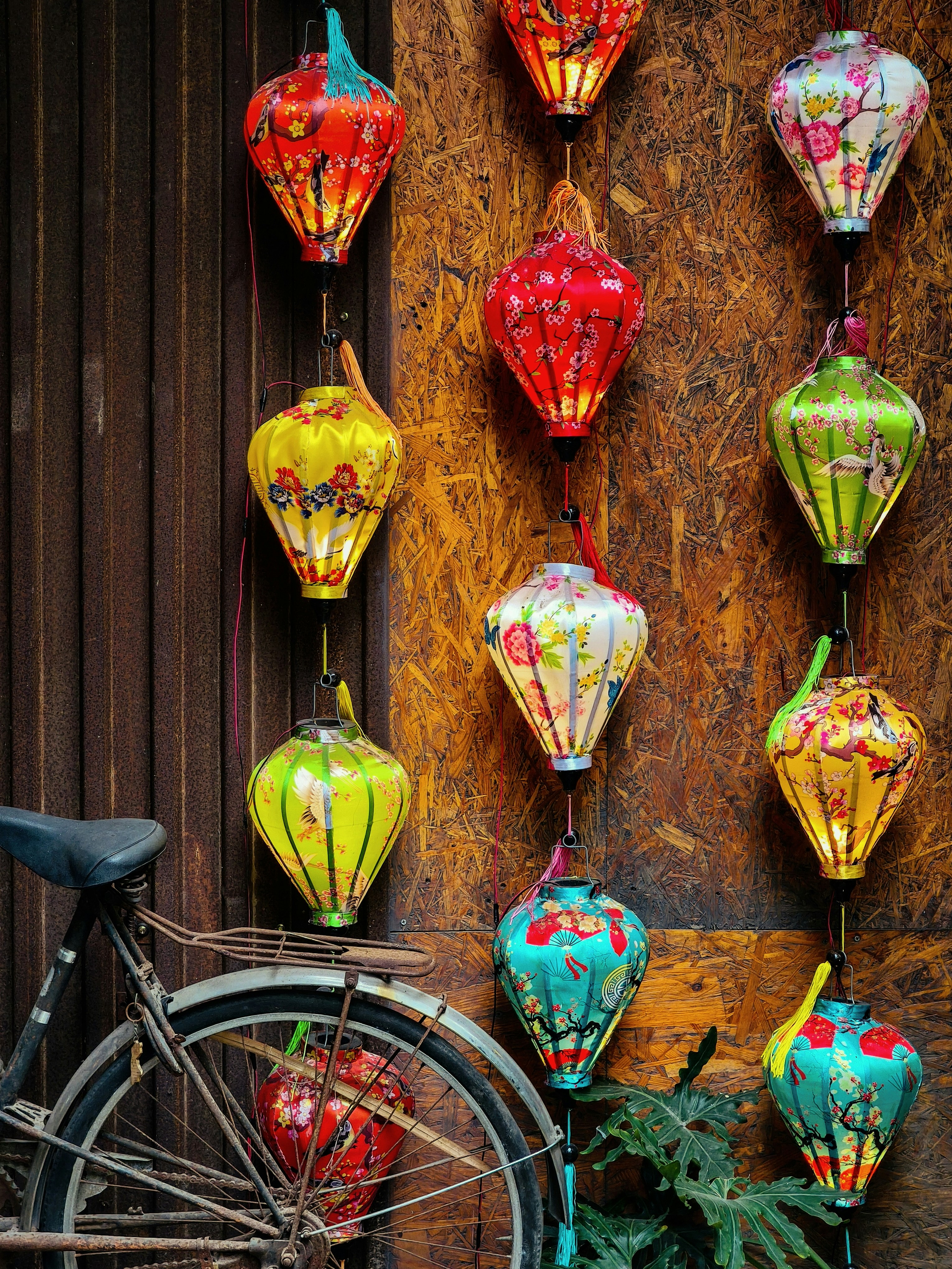 Colorful silk lanterns hanging on a wooden wall beside an old bicycle