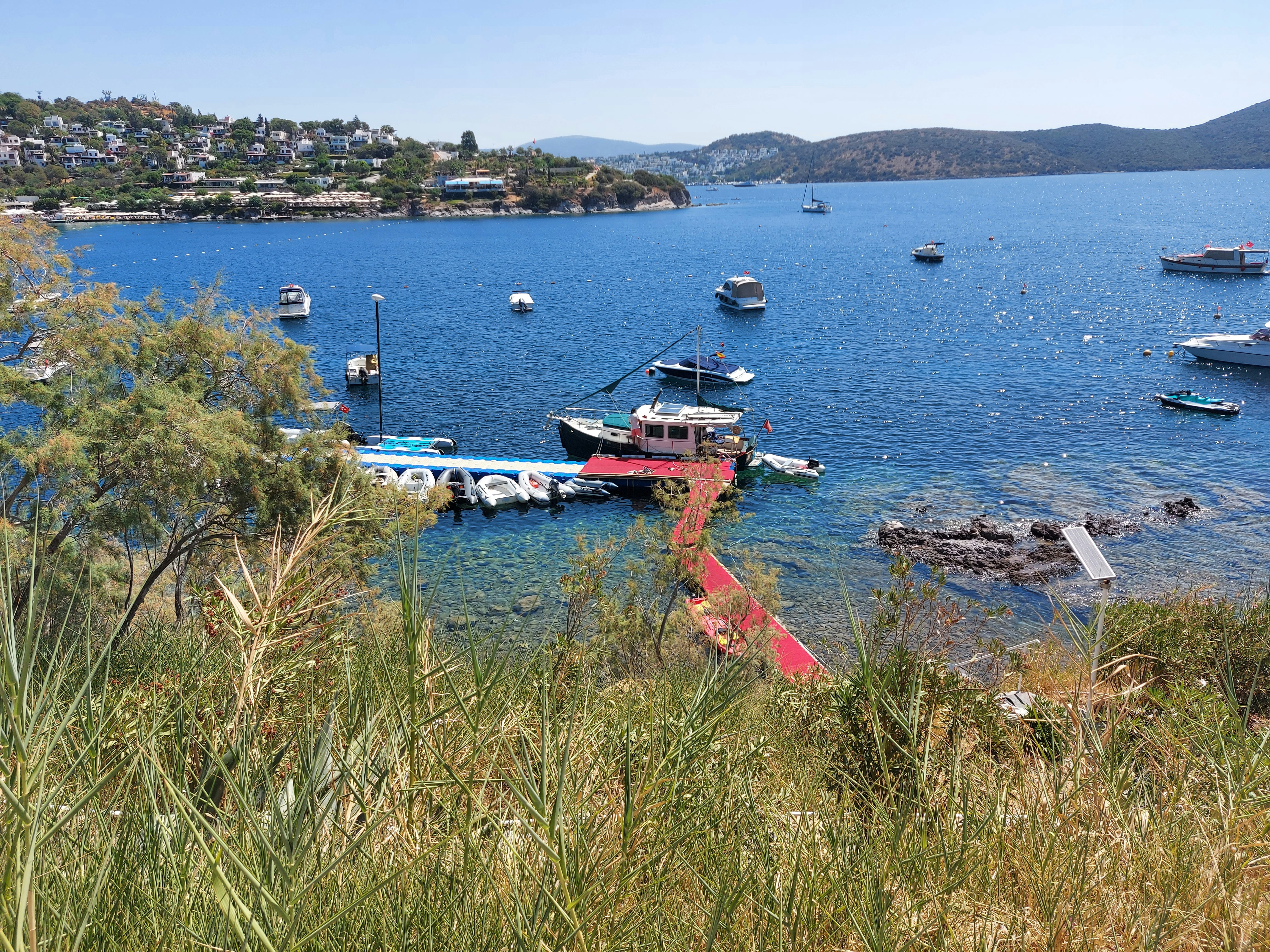 Boats moored at a red floating dock in a blue coastal bay