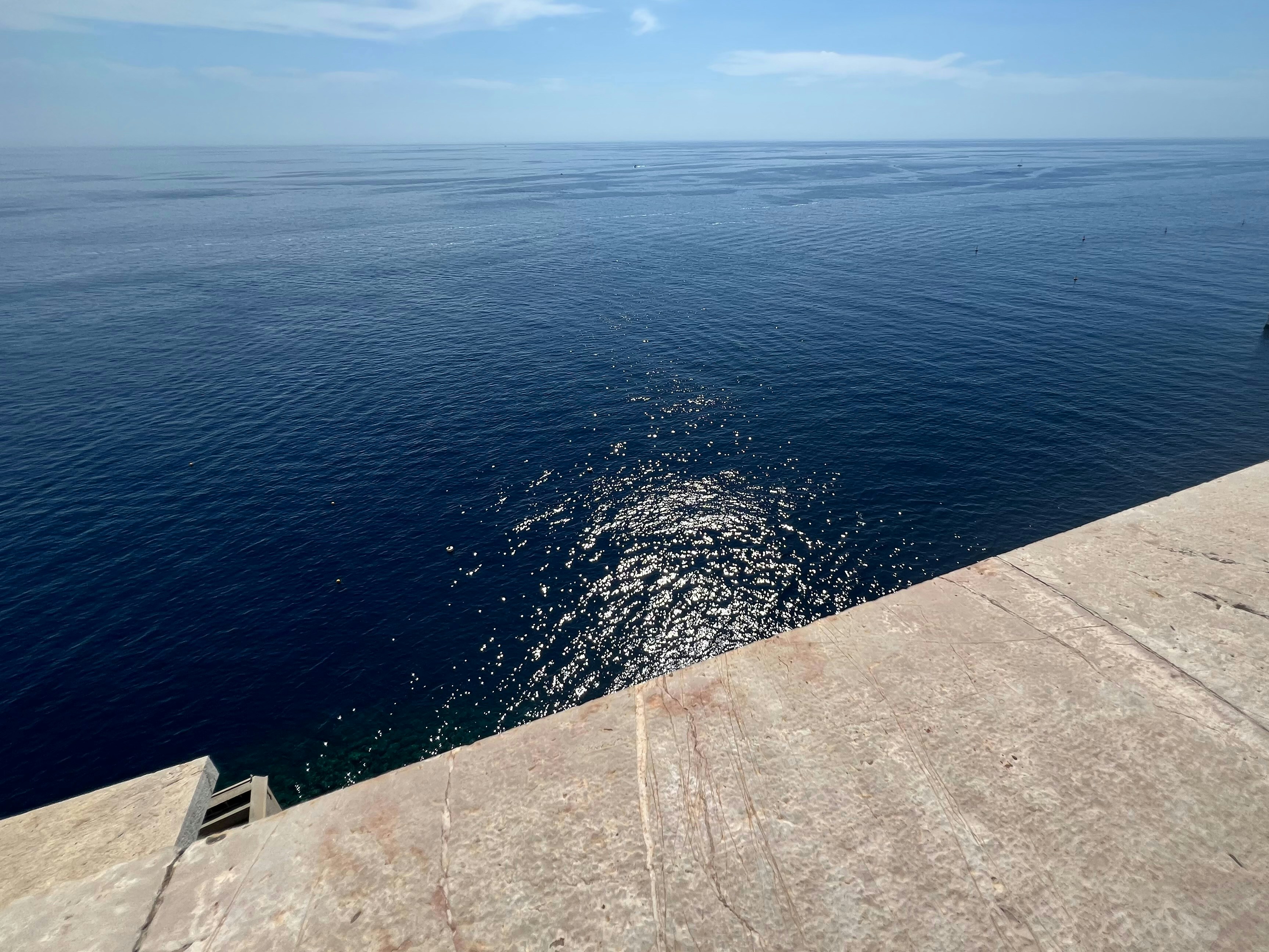 Sunlight reflecting on the deep blue sea from a stone ledge