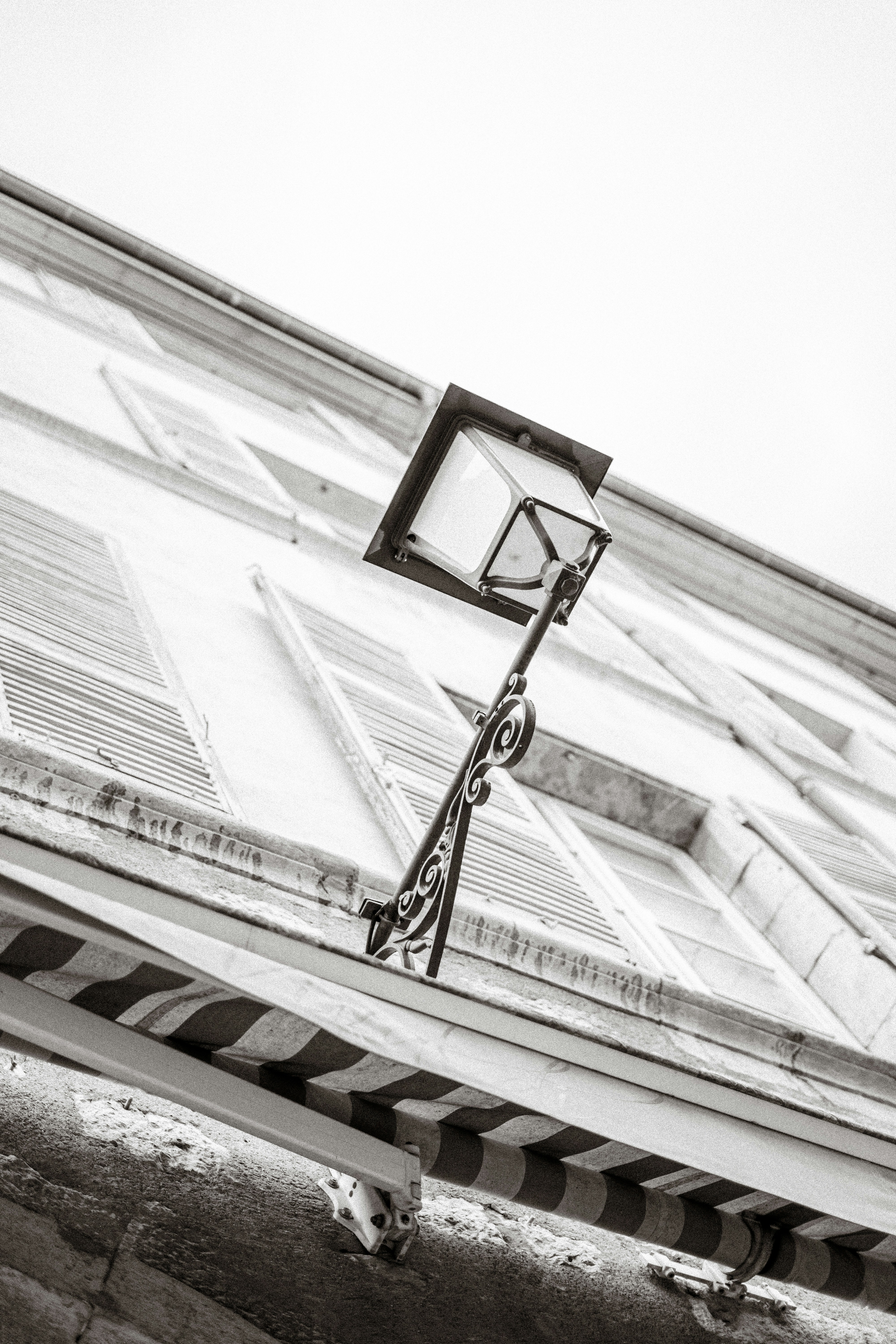 A black and white view of an ornate metal street lamp on a building facade