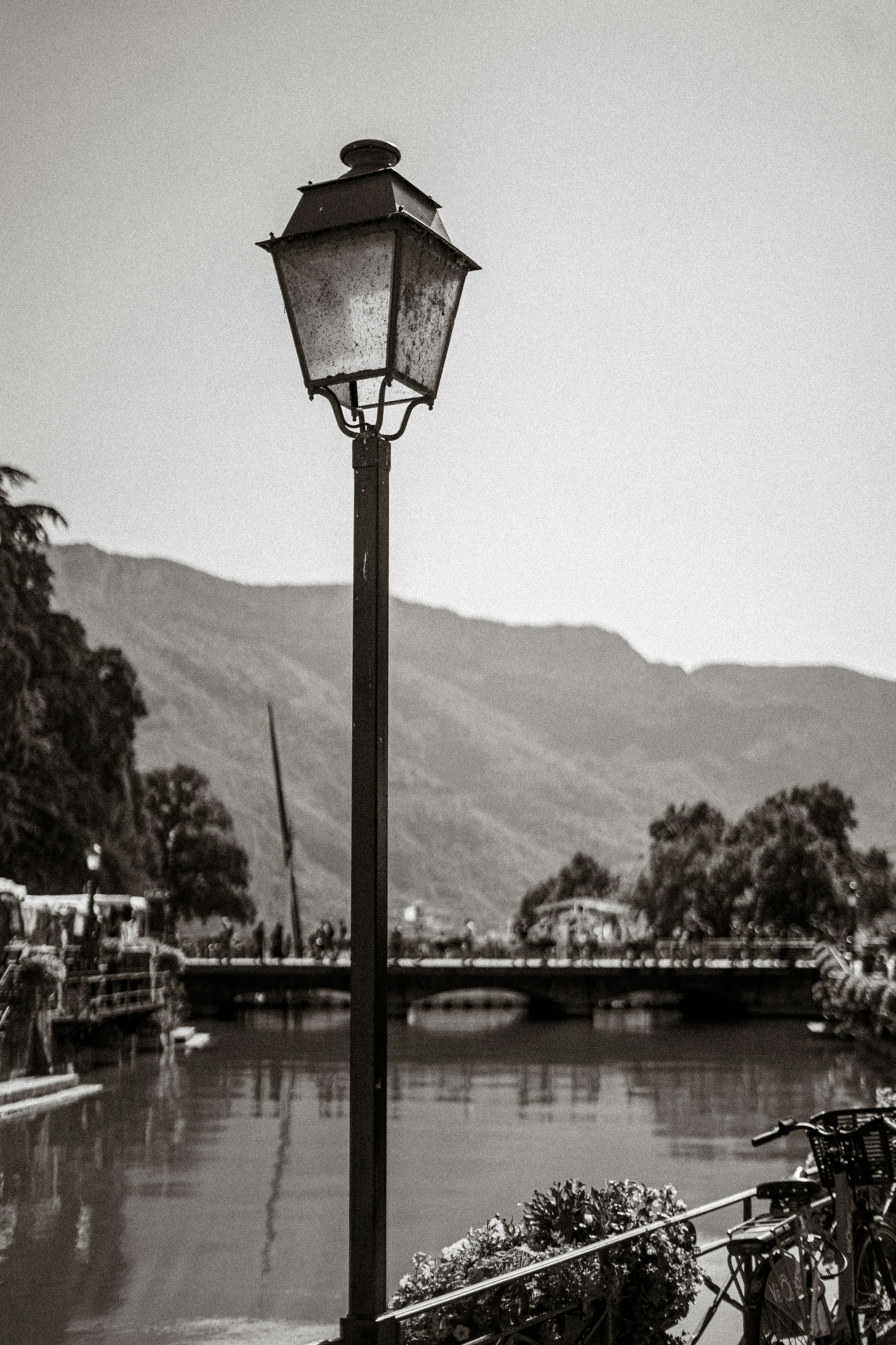 A vintage street lamp on a canal bank with a bridge and mountains