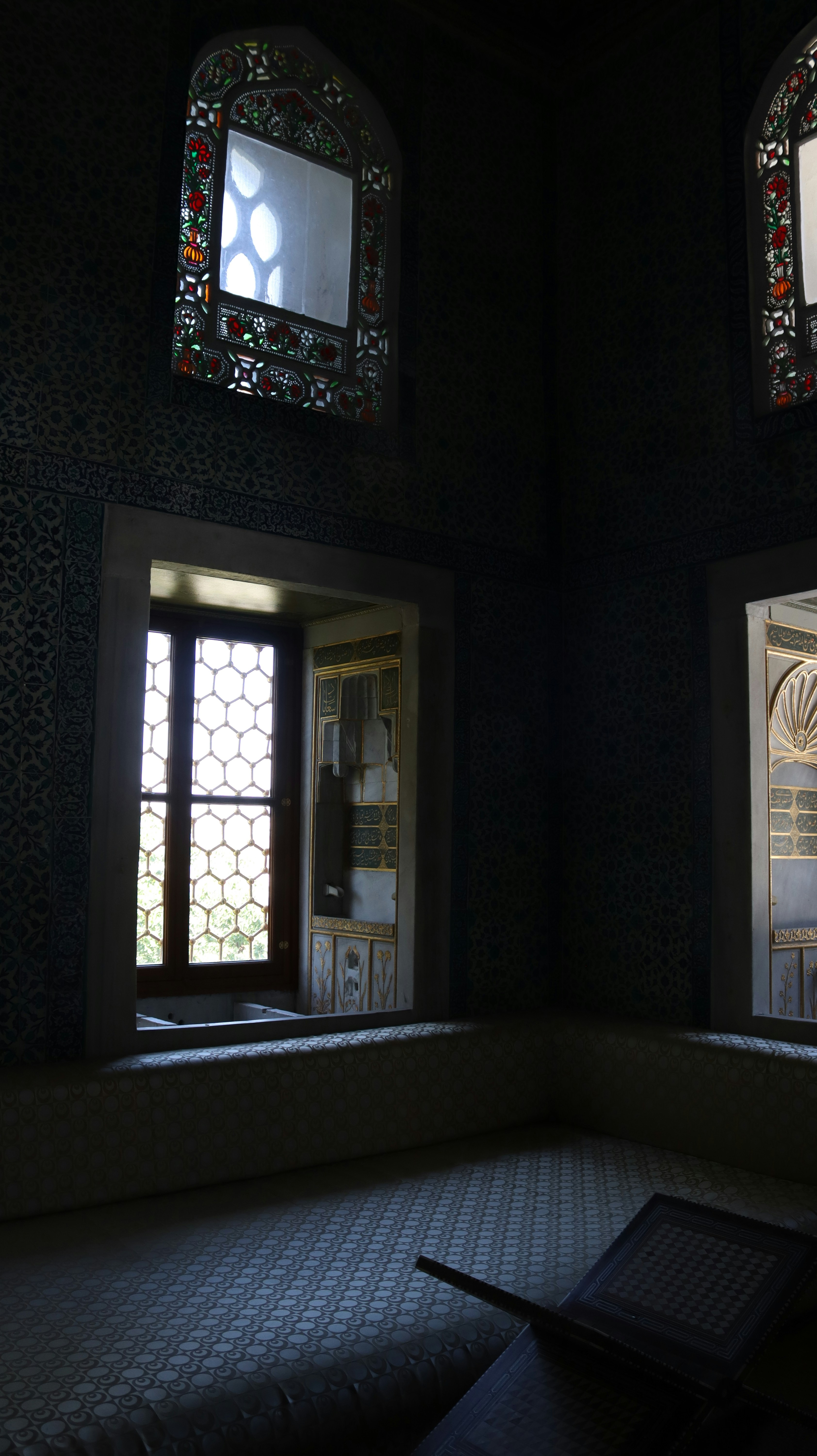 Dim room with ornate stained glass windows and tiled walls in Topkapi Palace