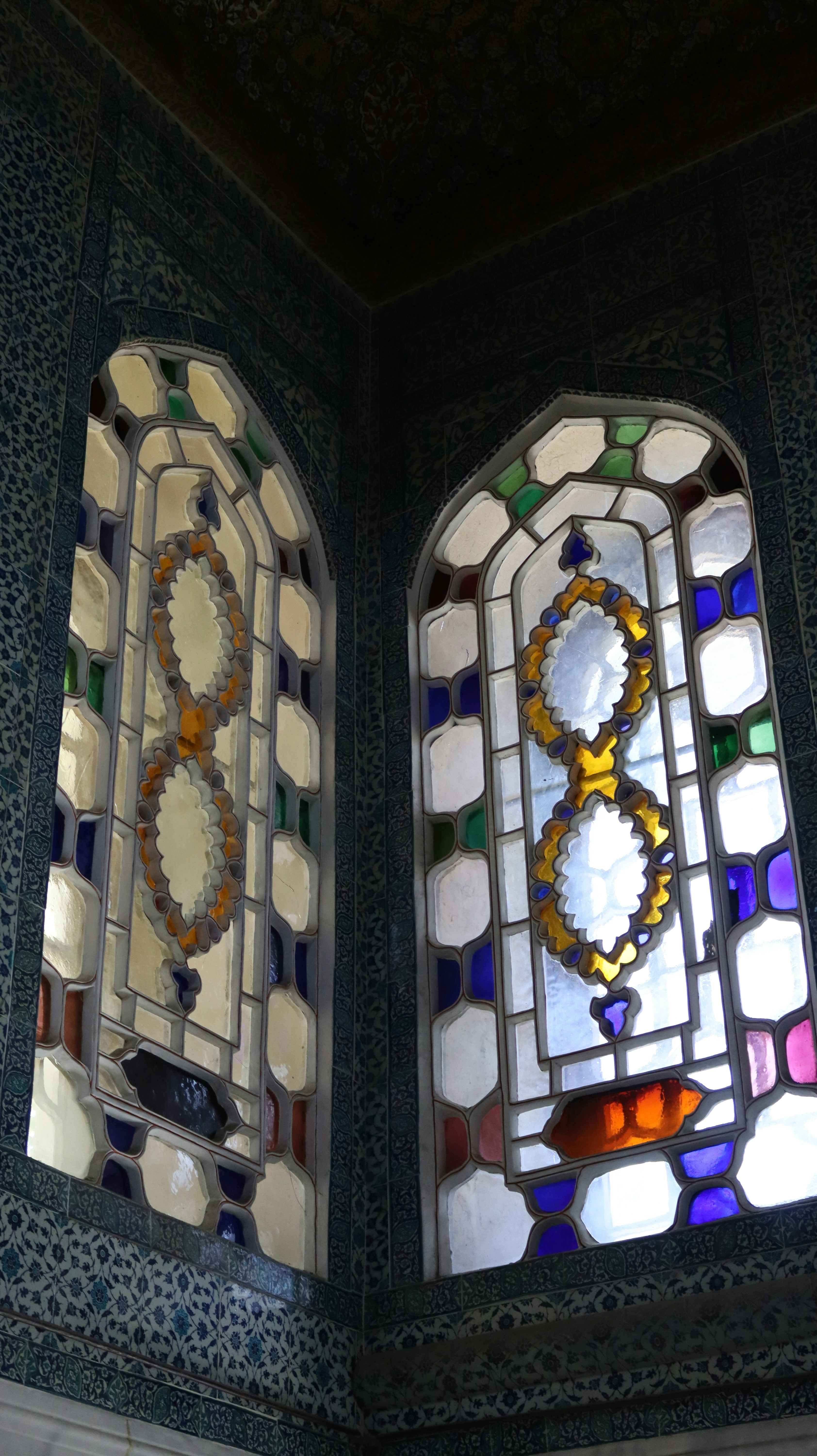 Two arched windows with intricate stained glass patterns set in a tiled corner