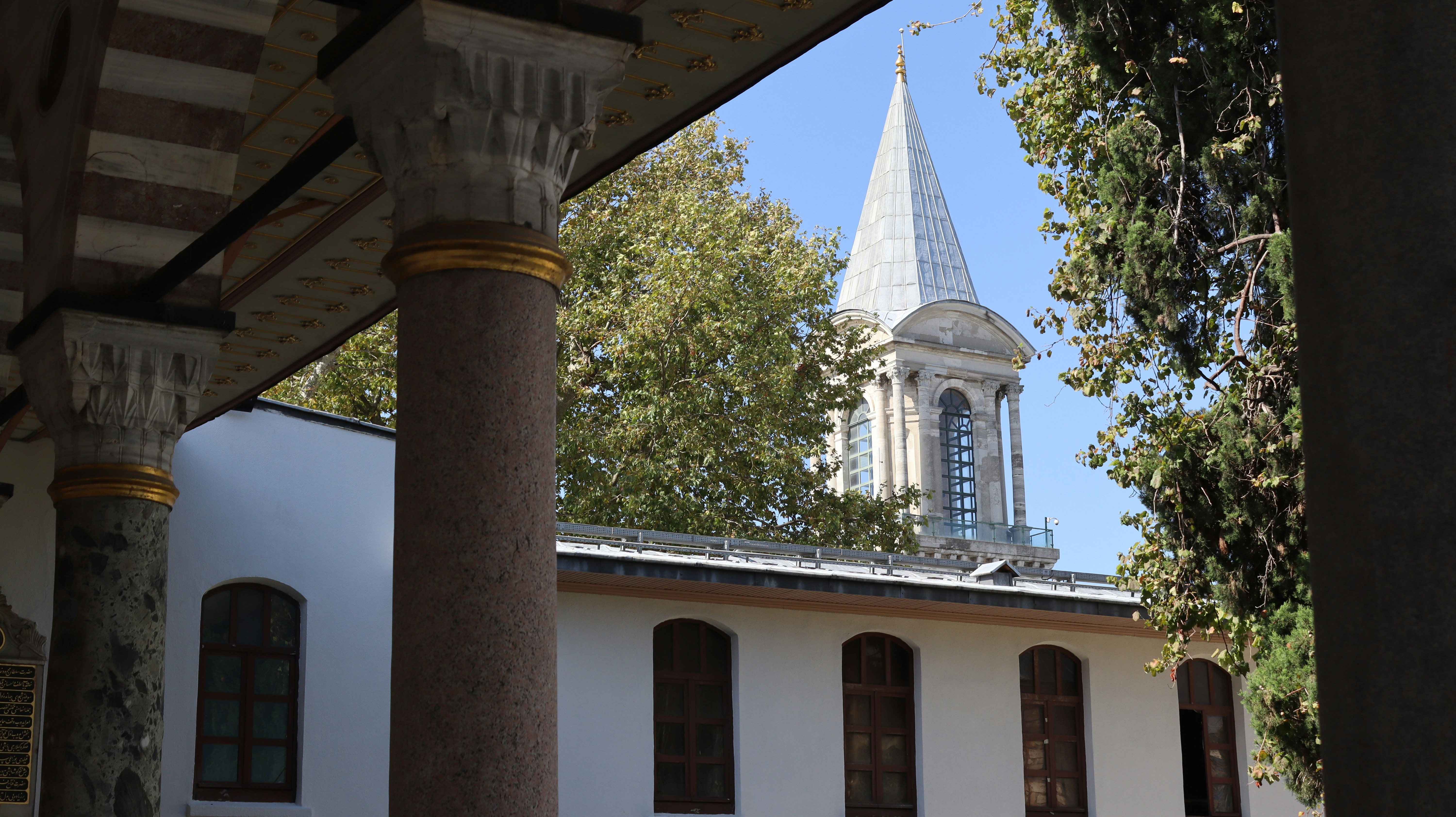 A stone tower with a conical roof rising above white buildings and trees
