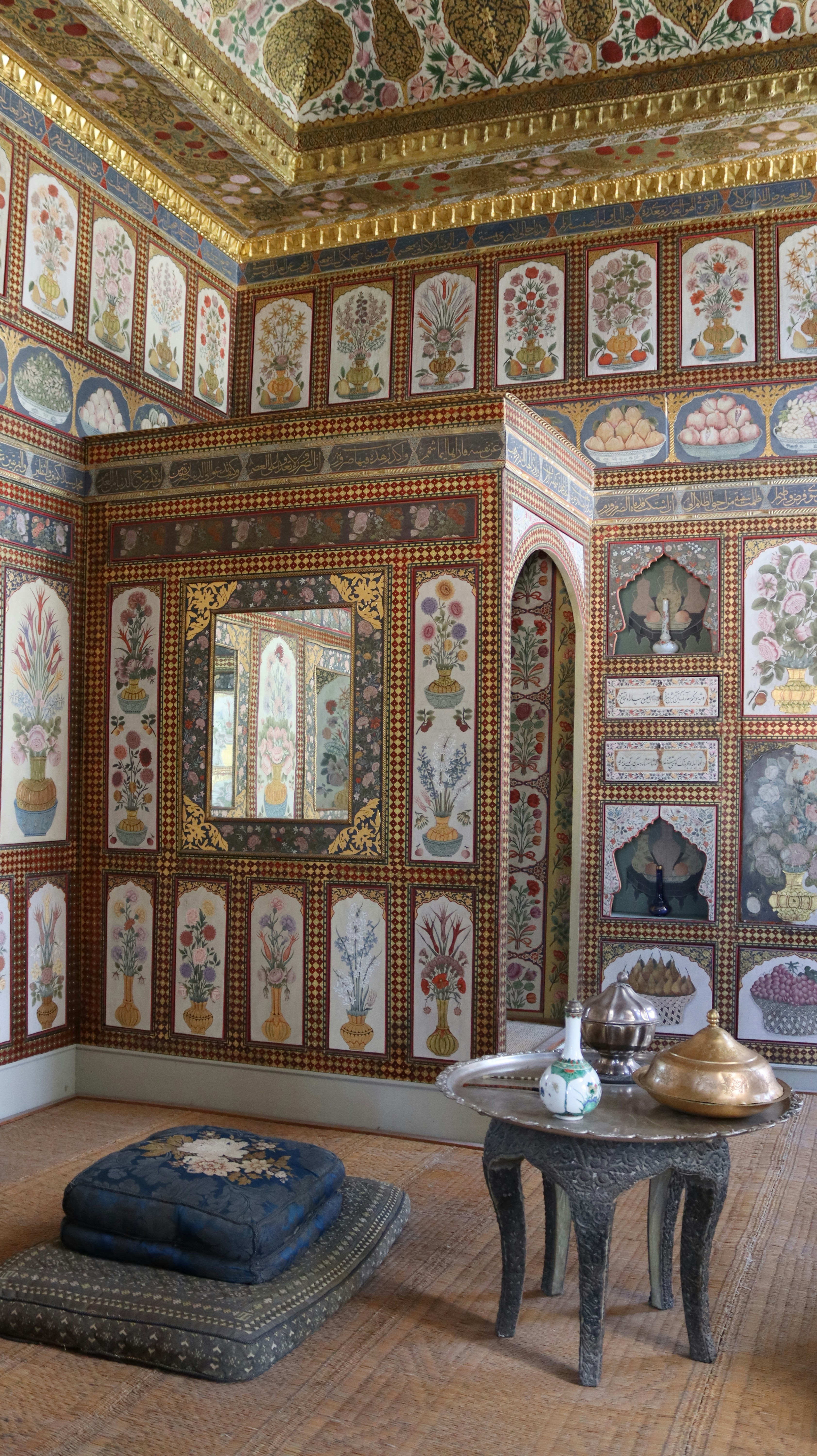 Ornate floral wall paintings and a metal table with vessels in a room