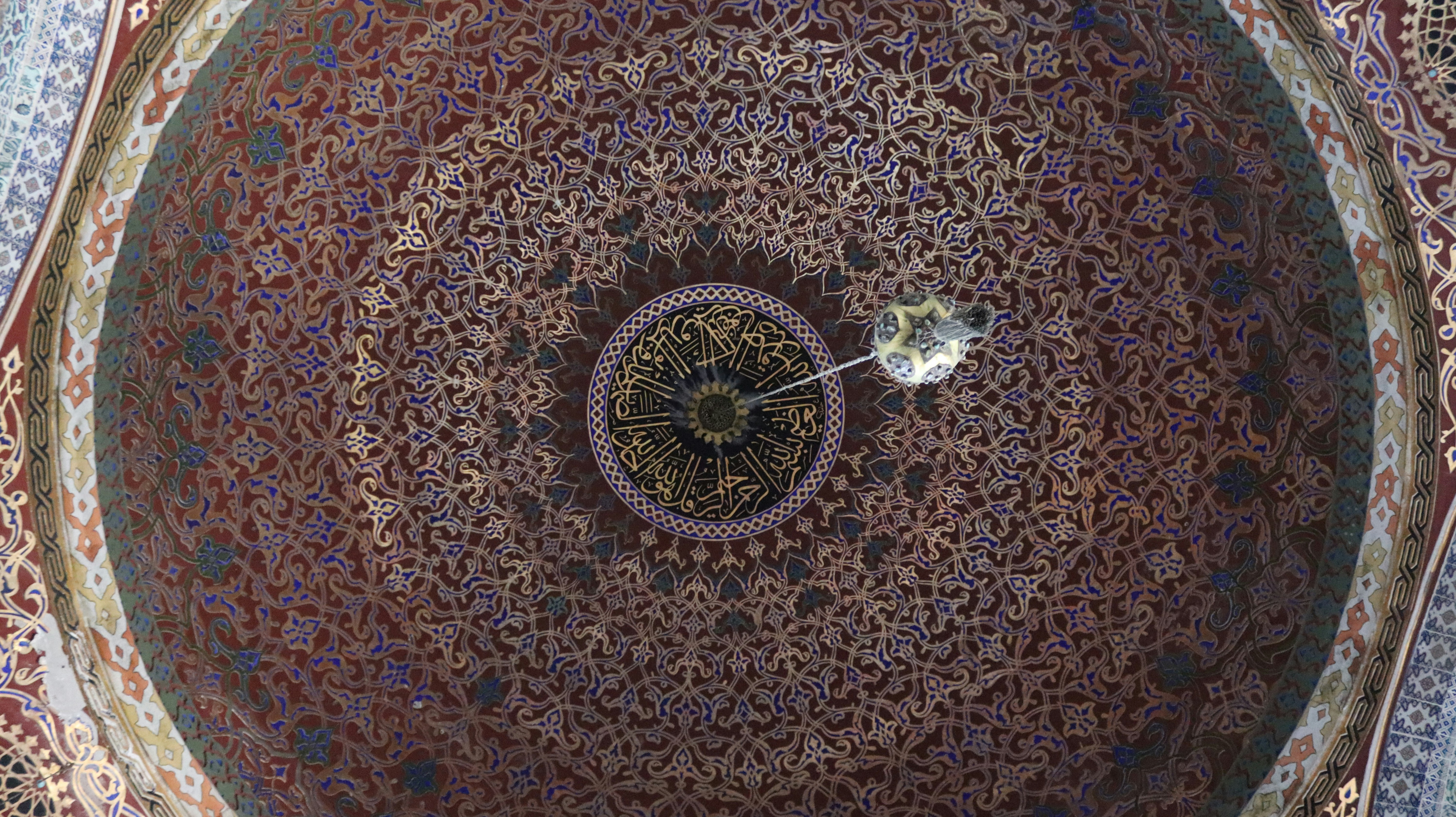 Intricate red and gold geometric patterns on a domed ceiling with central calligraphy